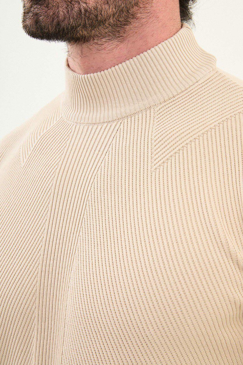Men’s beige slim-fit ribbed mock-neck cotton-blend sweater with multi-directional ribbing and diagonal chest panels, styled with dark trousers.