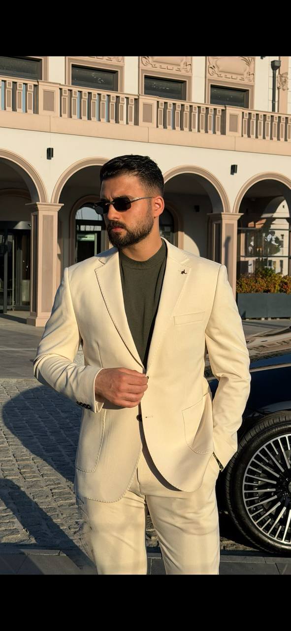 man wearing a beige two-piece slim-fit suit with a matching blazer and trousers, paired with olive loafers.