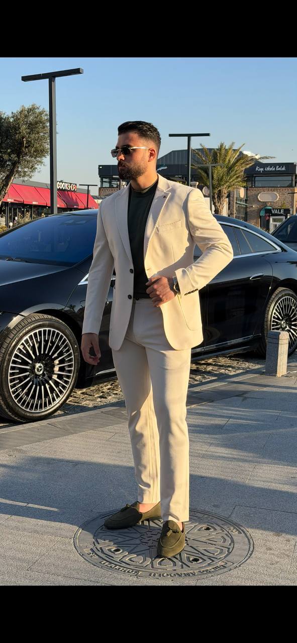 man wearing a beige two-piece slim-fit suit with a matching blazer and trousers, paired with olive loafers.
