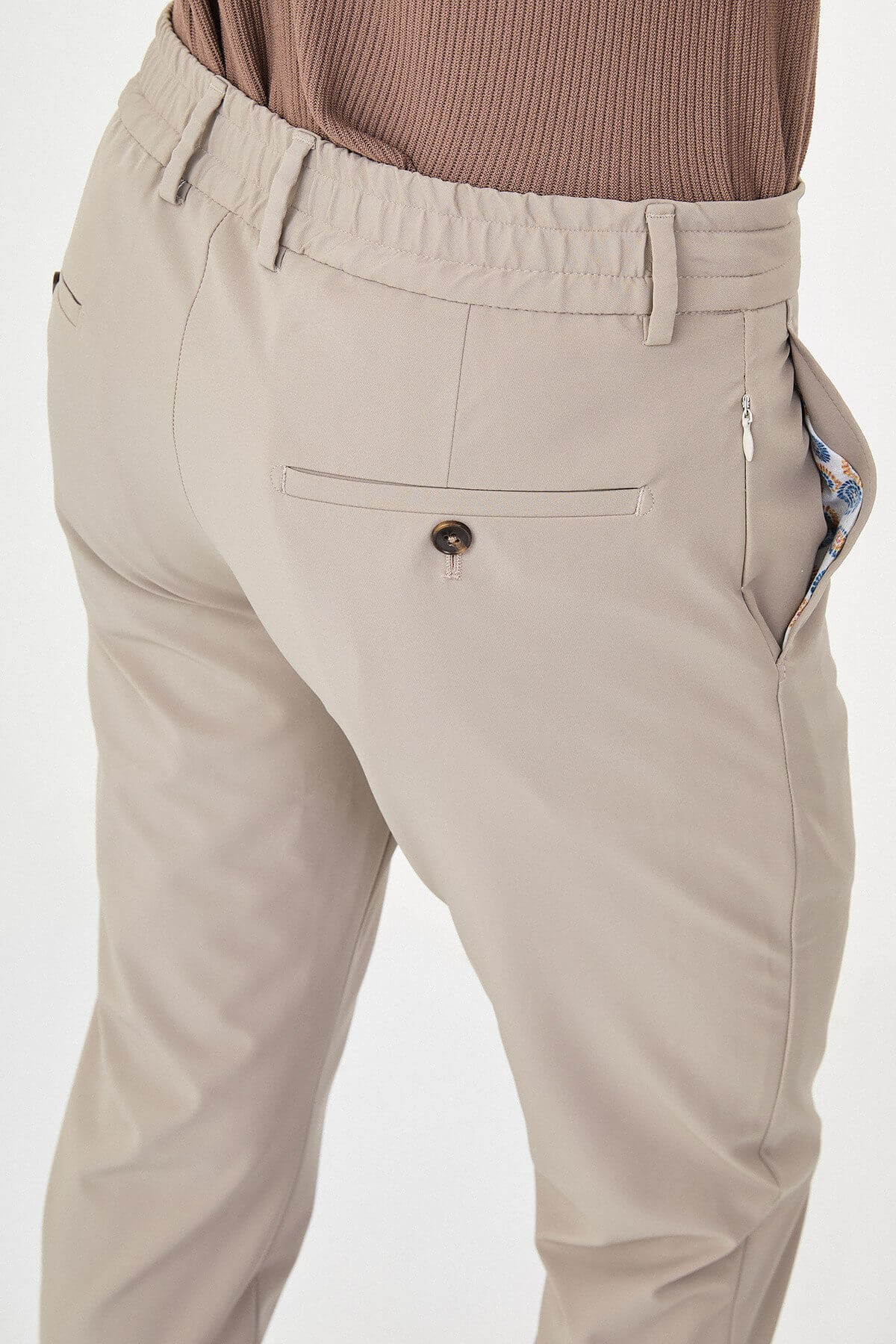 Man wearing beige slim-fit summer trousers, styled with a navy polo shirt and white sneakers, standing against a neutral background.