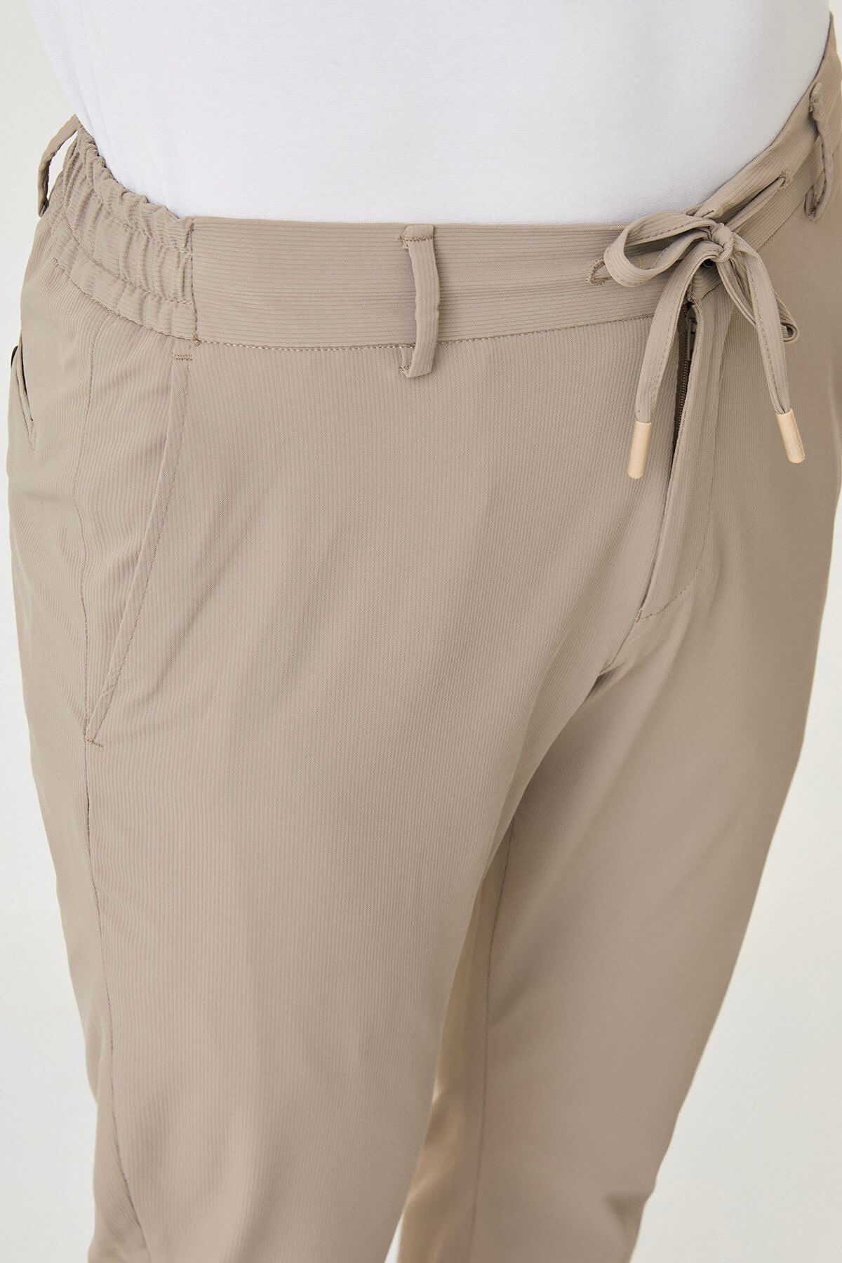 Man wearing beige slim-fit summer trousers styled with white sneakers and a white polo shirt.