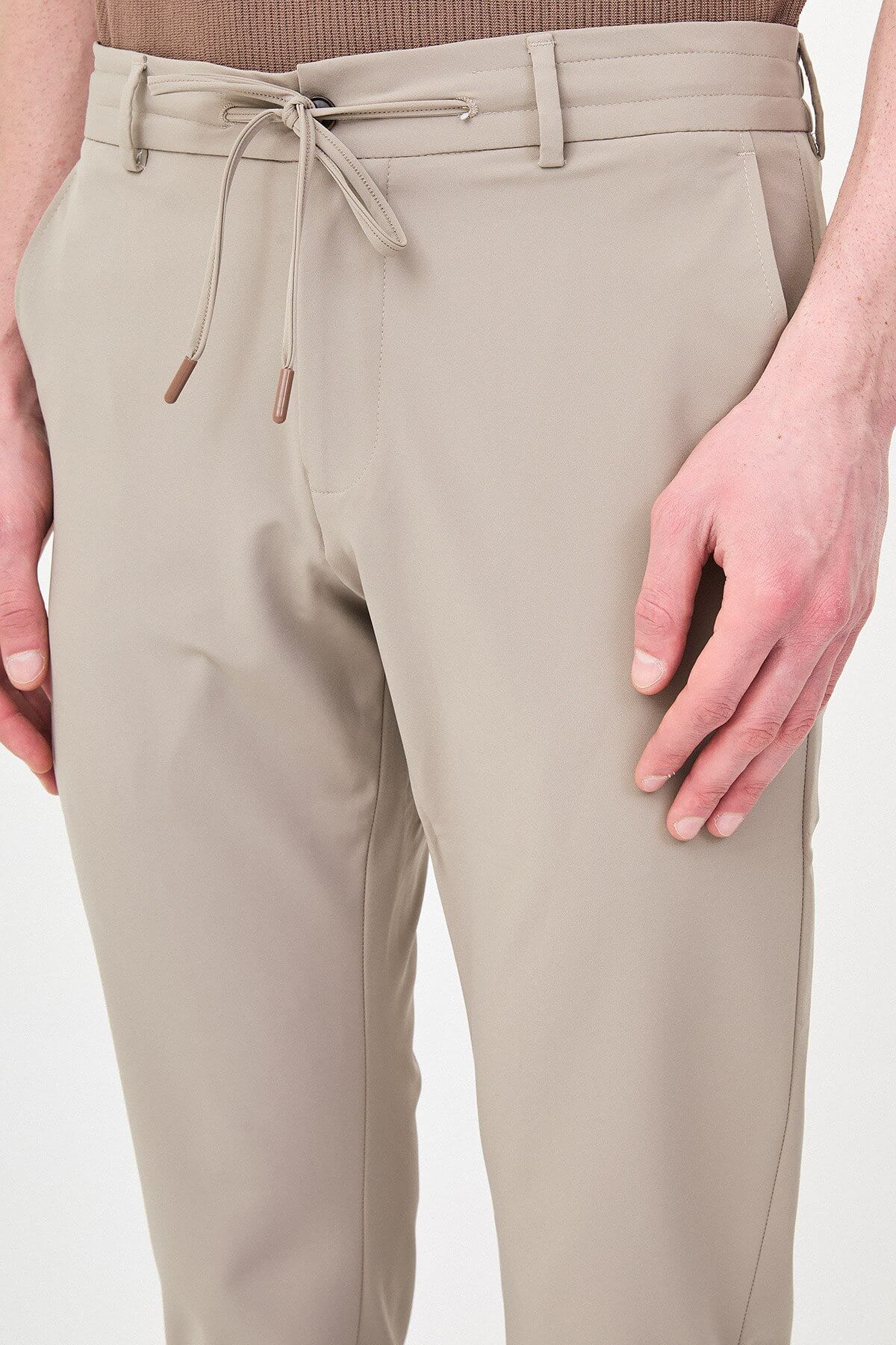 Man wearing beige slim-fit summer trousers, styled with a navy polo shirt and white sneakers, standing against a neutral background.