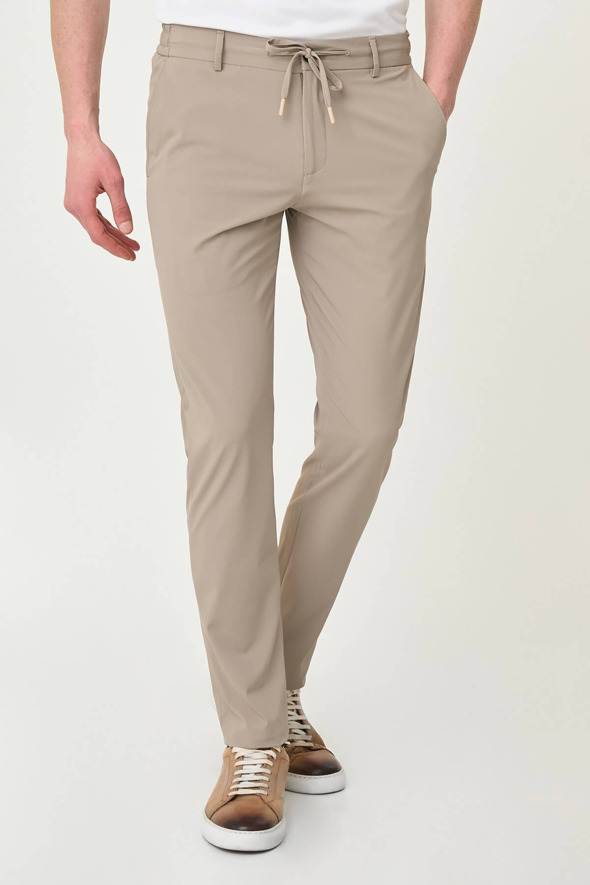 Man wearing beige slim-fit summer trousers styled with white sneakers and a white polo shirt.