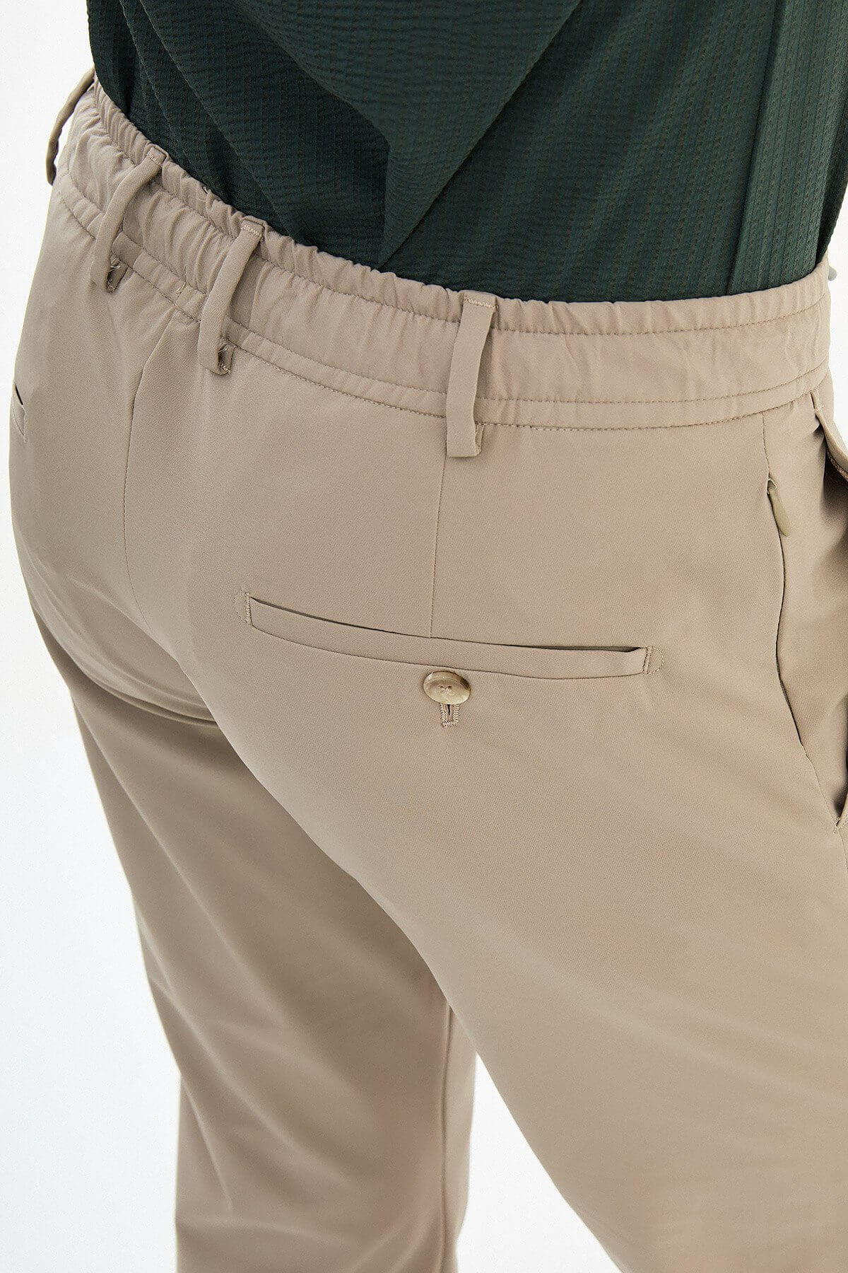 Man wearing beige slim-fit summer trousers, styled with a navy polo shirt and white sneakers, standing against a neutral background.