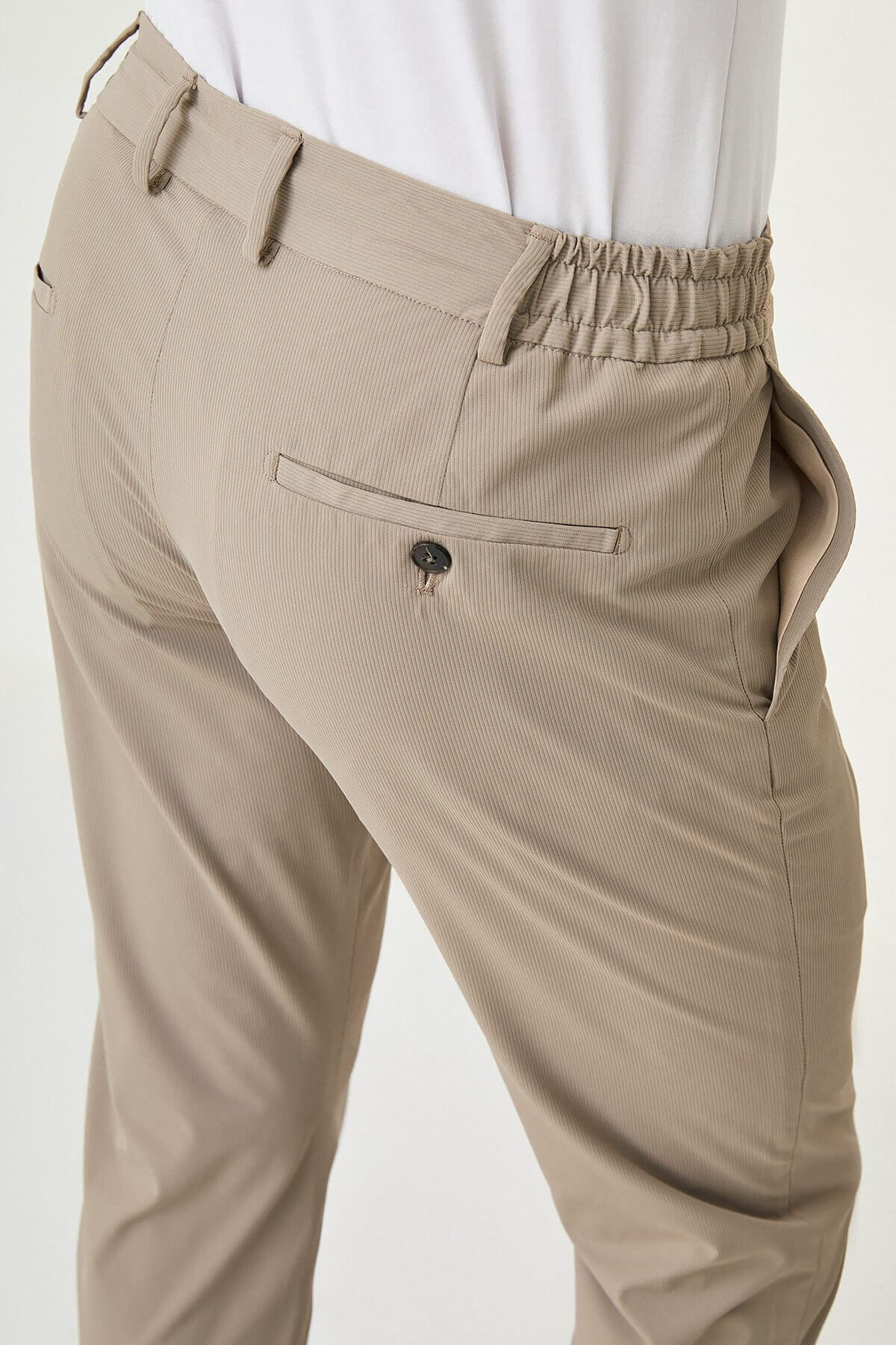 Man wearing beige slim-fit summer trousers styled with white sneakers and a white polo shirt.