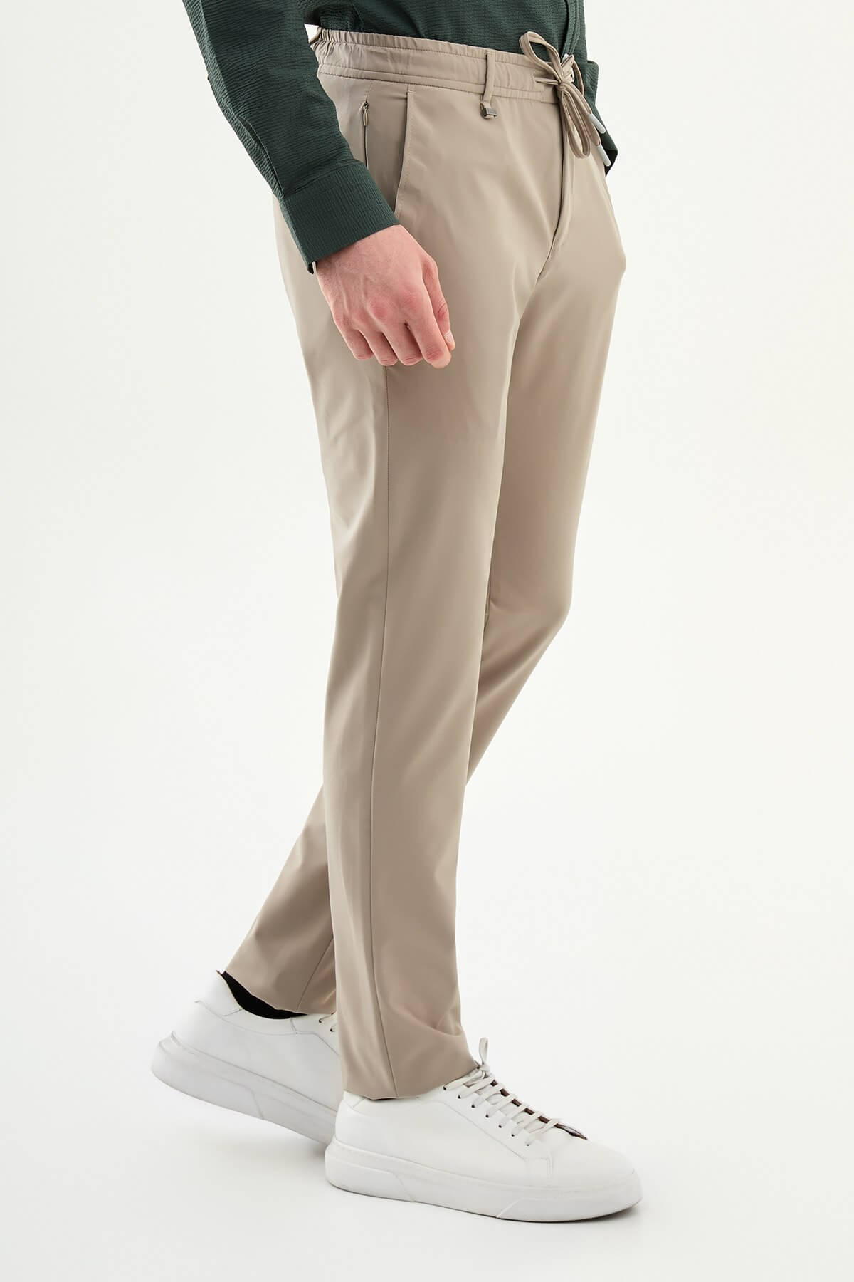 Man wearing beige slim-fit summer trousers, styled with a navy polo shirt and white sneakers, standing against a neutral background.