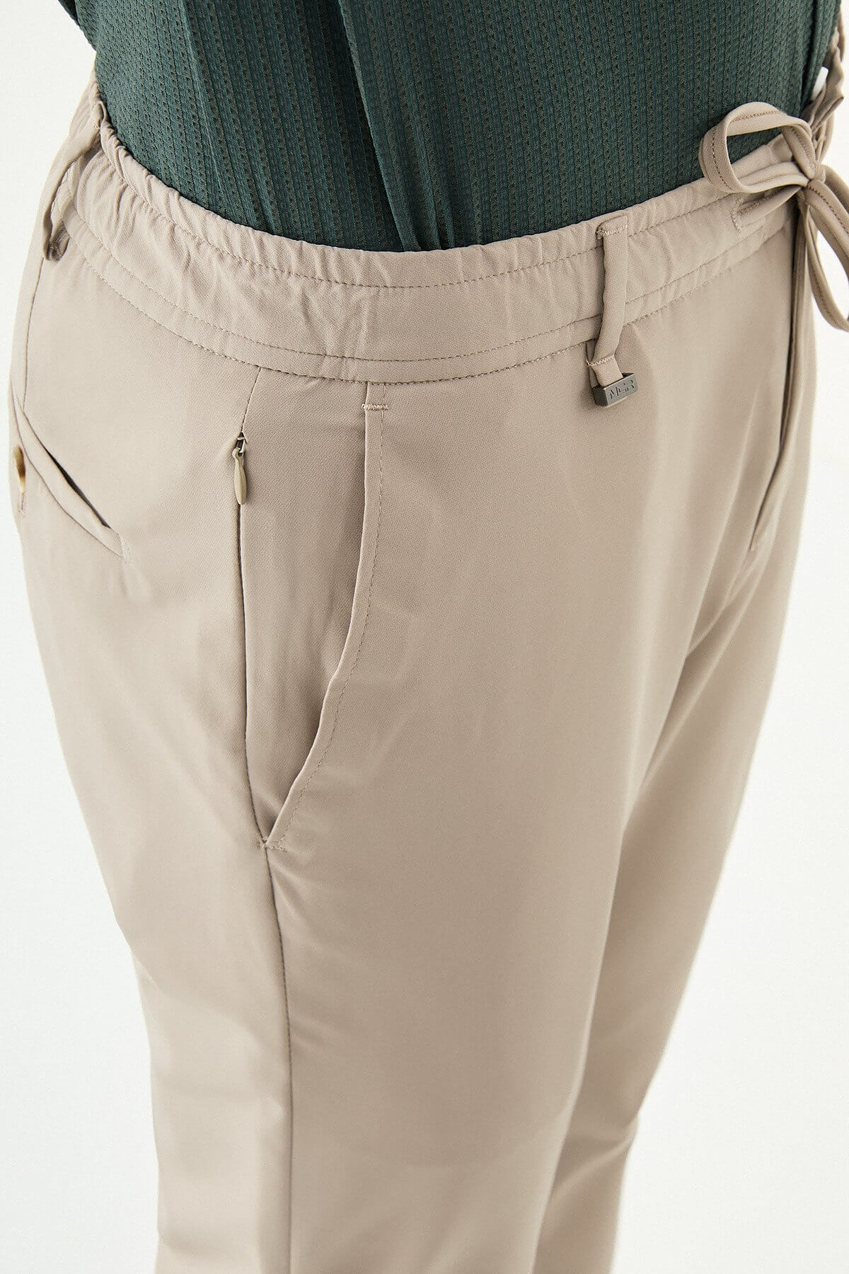 Man wearing beige slim-fit summer trousers, styled with a navy polo shirt and white sneakers, standing against a neutral background.