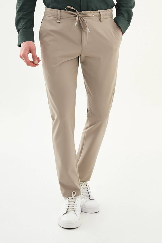 Man wearing beige slim-fit summer trousers, styled with a navy polo shirt and white sneakers, standing against a neutral background.
