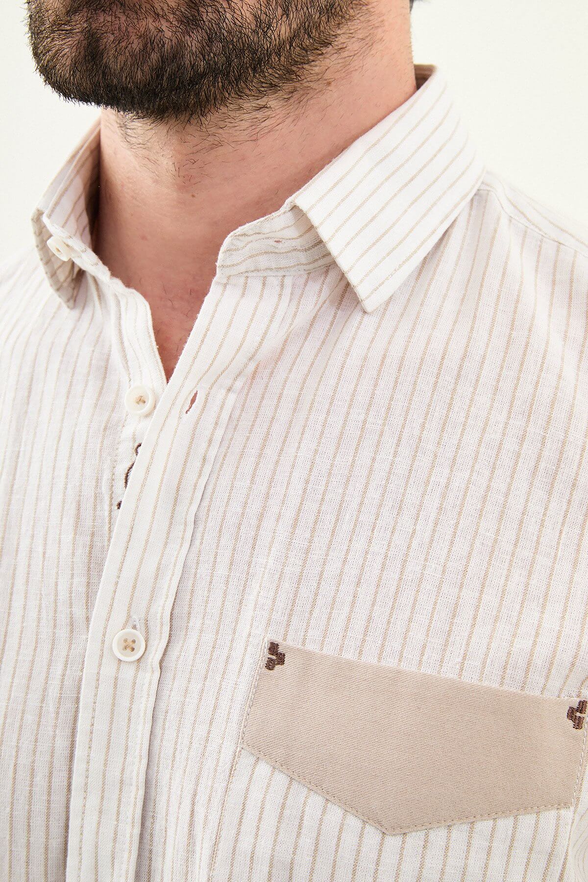 beige slim-fit long sleeve shirt with subtle stripe detailing, pocket accent, and tailored cuffs, paired with light trousers