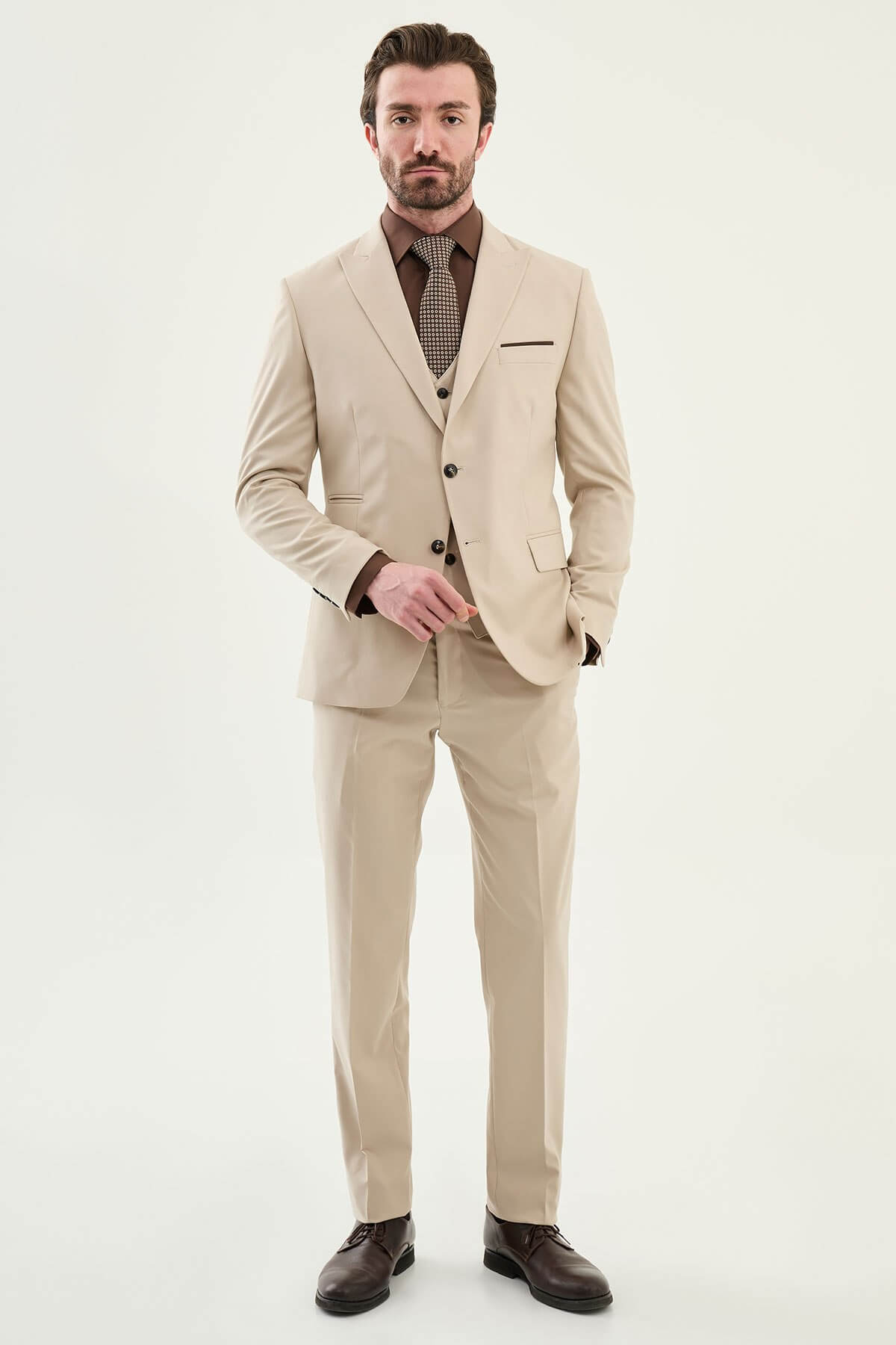 Beige slim-fit three-piece men’s suit with brown shirt and patterned tie