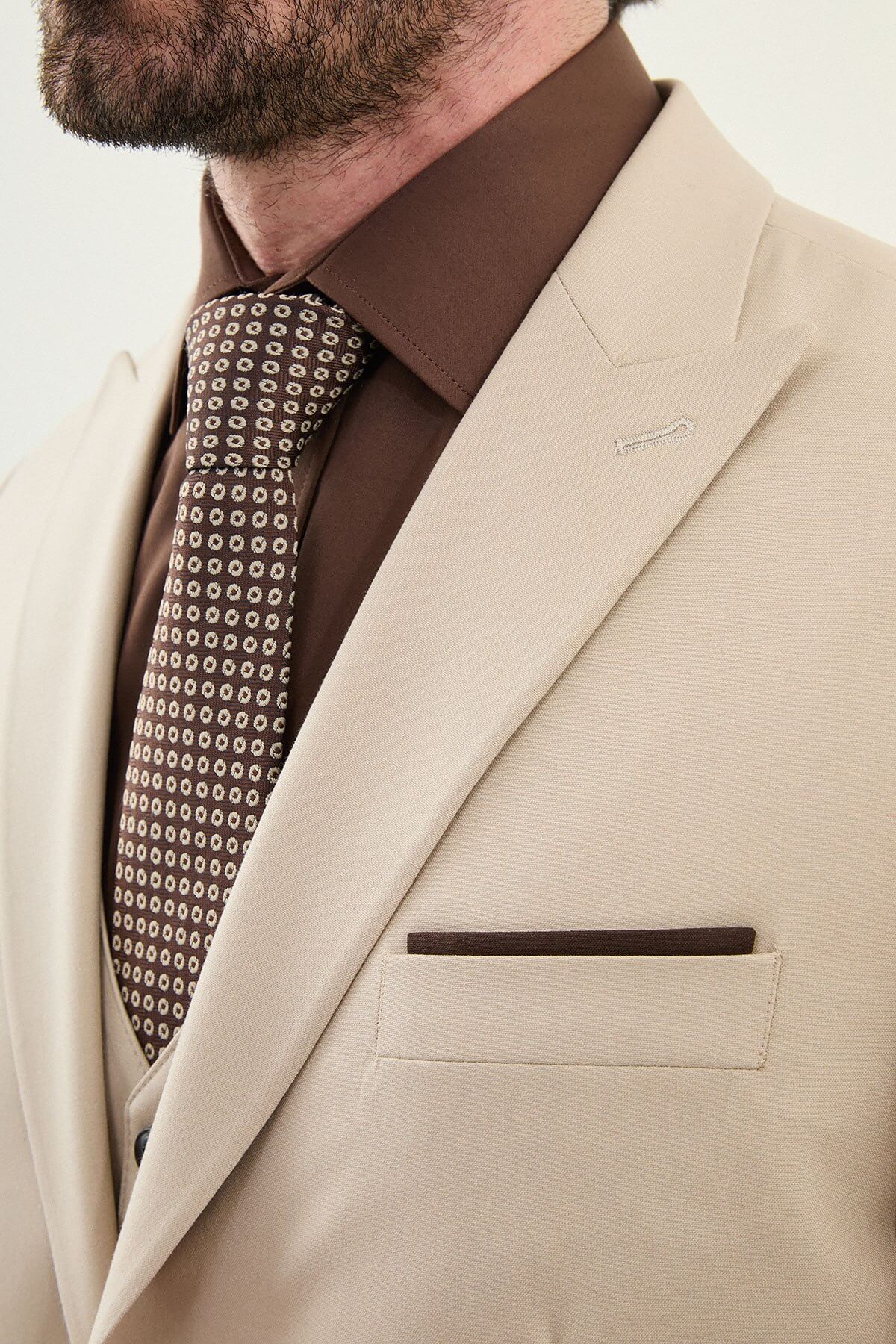 Beige slim-fit three-piece men’s suit with brown shirt and patterned tie