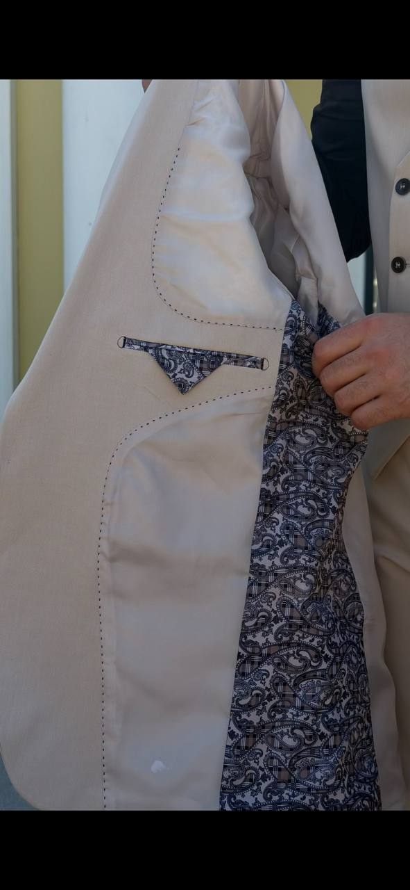 beige three-piece slim-fit suit showing the tailored jacket and waistcoat details with black shirt, highlighting the fabric texture and fit.