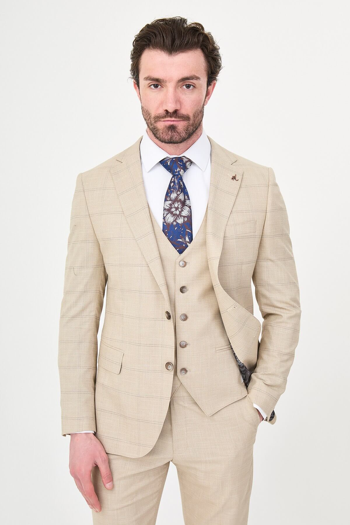 a beige check slim-fit three-piece suit with matching waistcoat and trousers, white dress shirt, patterned navy and brown tie, and dark brown leather shoes.