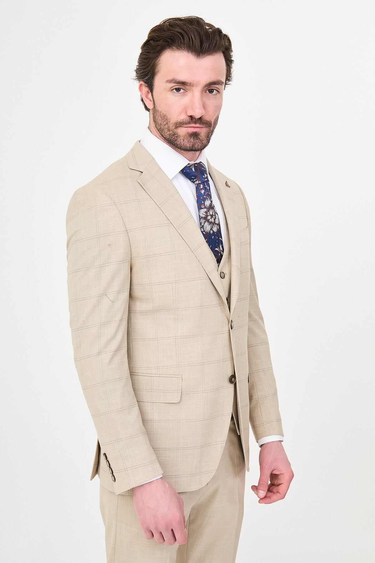 a beige check slim-fit three-piece suit with matching waistcoat and trousers, white dress shirt, patterned navy and brown tie, and dark brown leather shoes.