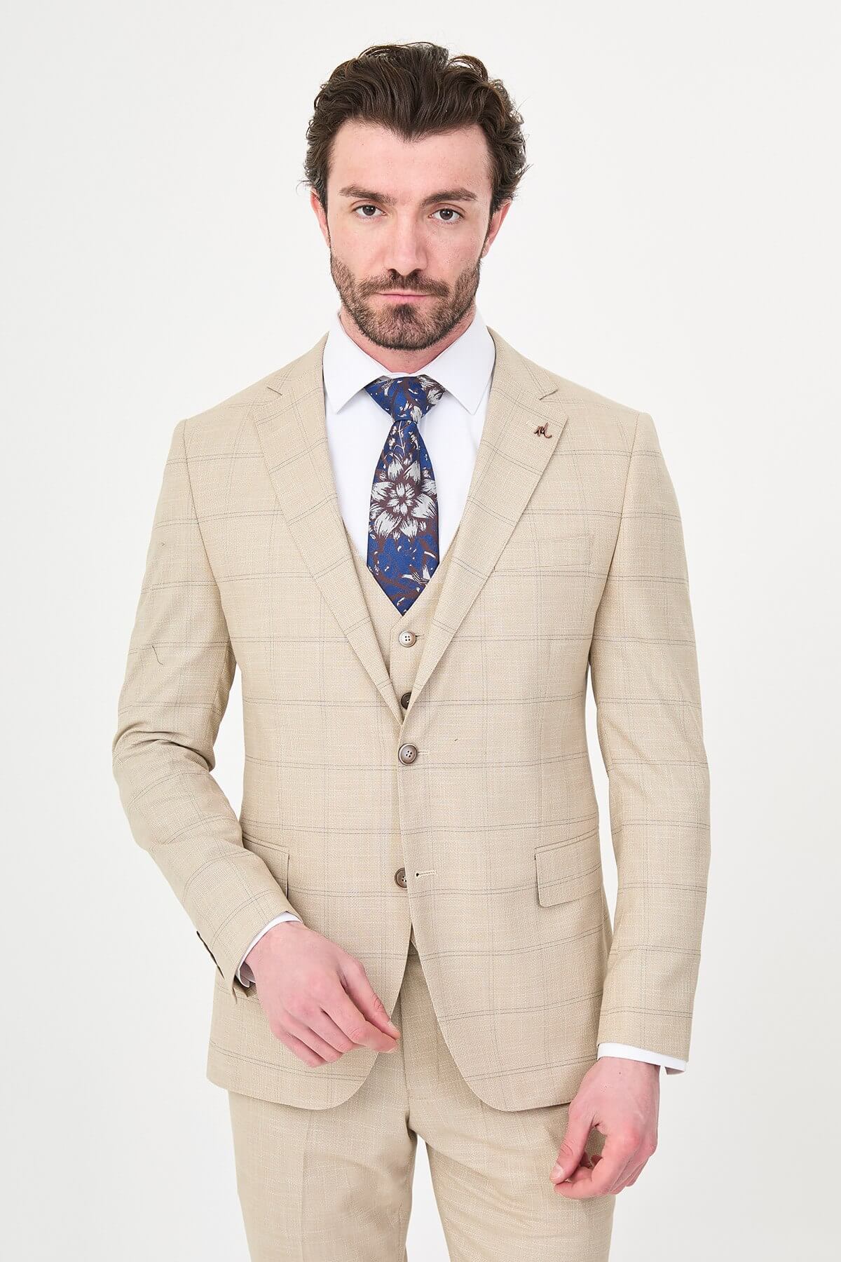 a beige check slim-fit three-piece suit with matching waistcoat and trousers, white dress shirt, patterned navy and brown tie, and dark brown leather shoes.