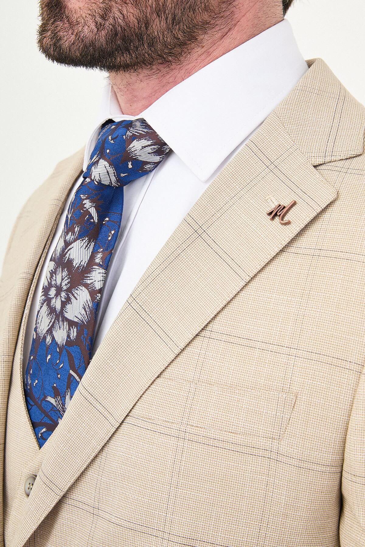 a beige check slim-fit three-piece suit with matching waistcoat and trousers, white dress shirt, patterned navy and brown tie, and dark brown leather shoes.