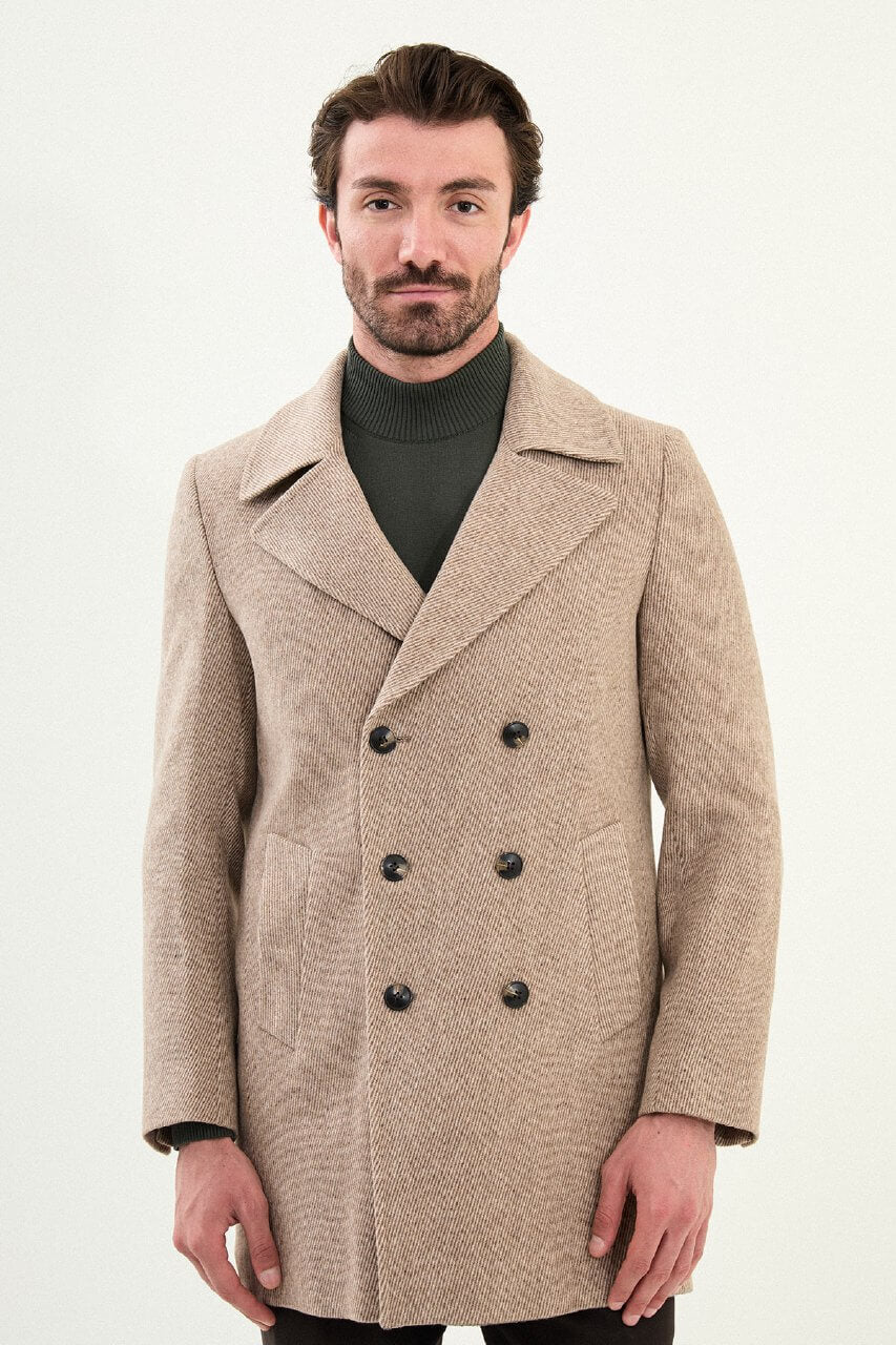 A man wearing a beige double-breasted slim fit peacoat with wide lapels, styled over a dark green turtleneck and paired with dark trousers