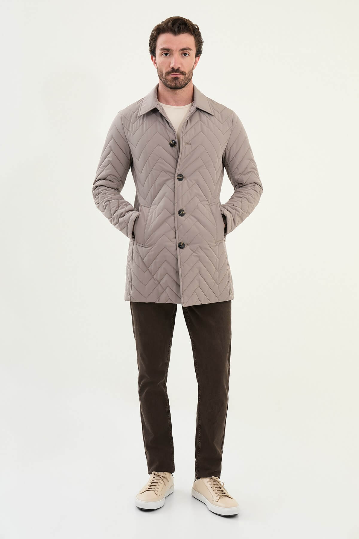 Men’s beige slim fit quilted coat with chevron stitching, styled with brown trousers and sneakers.