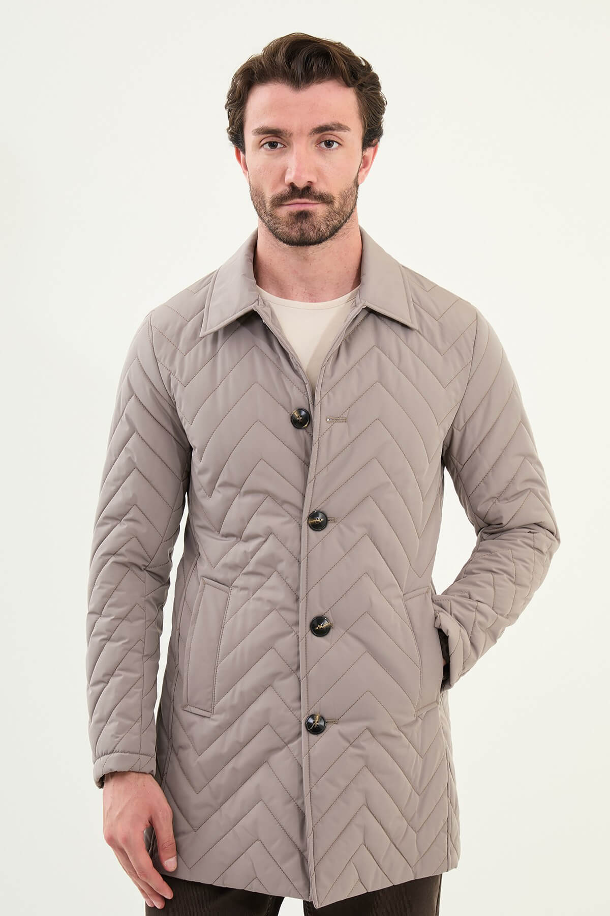 Men’s beige slim fit quilted coat with chevron stitching, styled with brown trousers and sneakers.