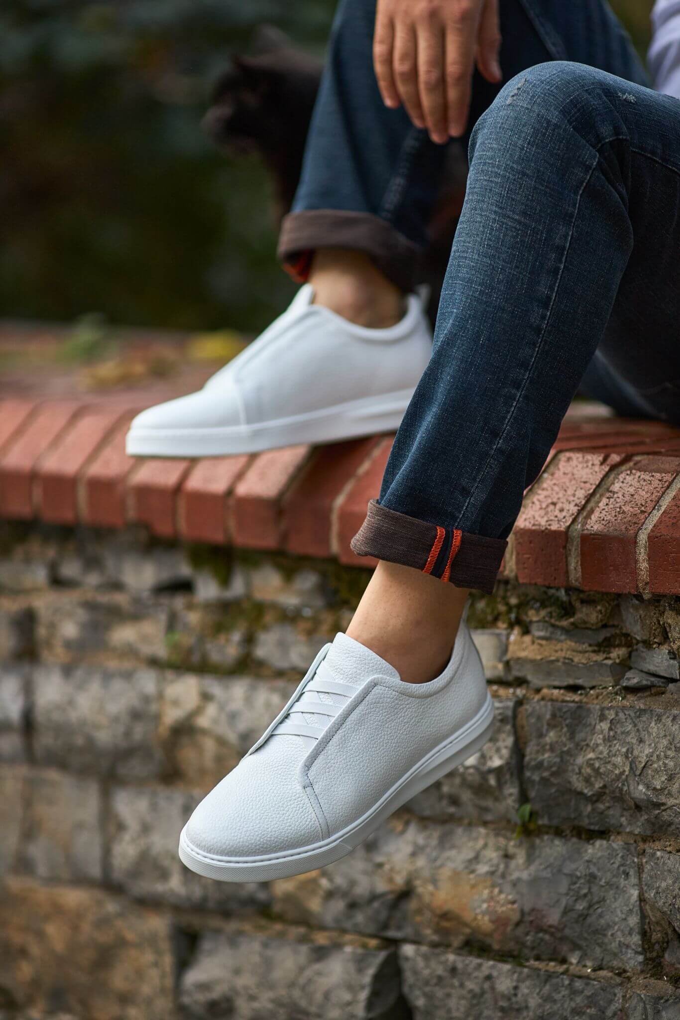Men’s white leather minimalist court sneaker styled with cuffed denim — premium casual footwear.