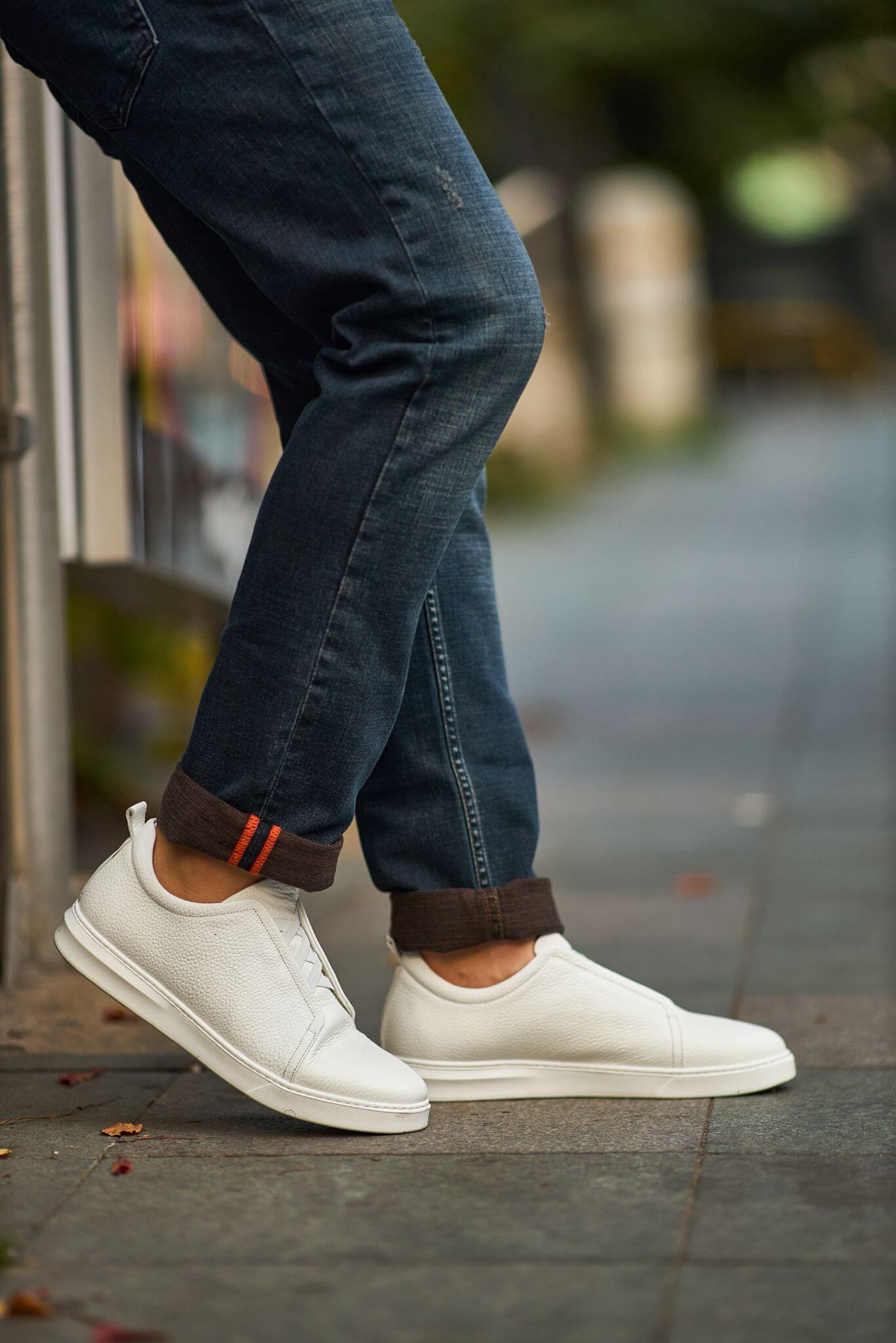 Men’s white leather minimalist court sneaker styled with cuffed denim — premium casual footwear.