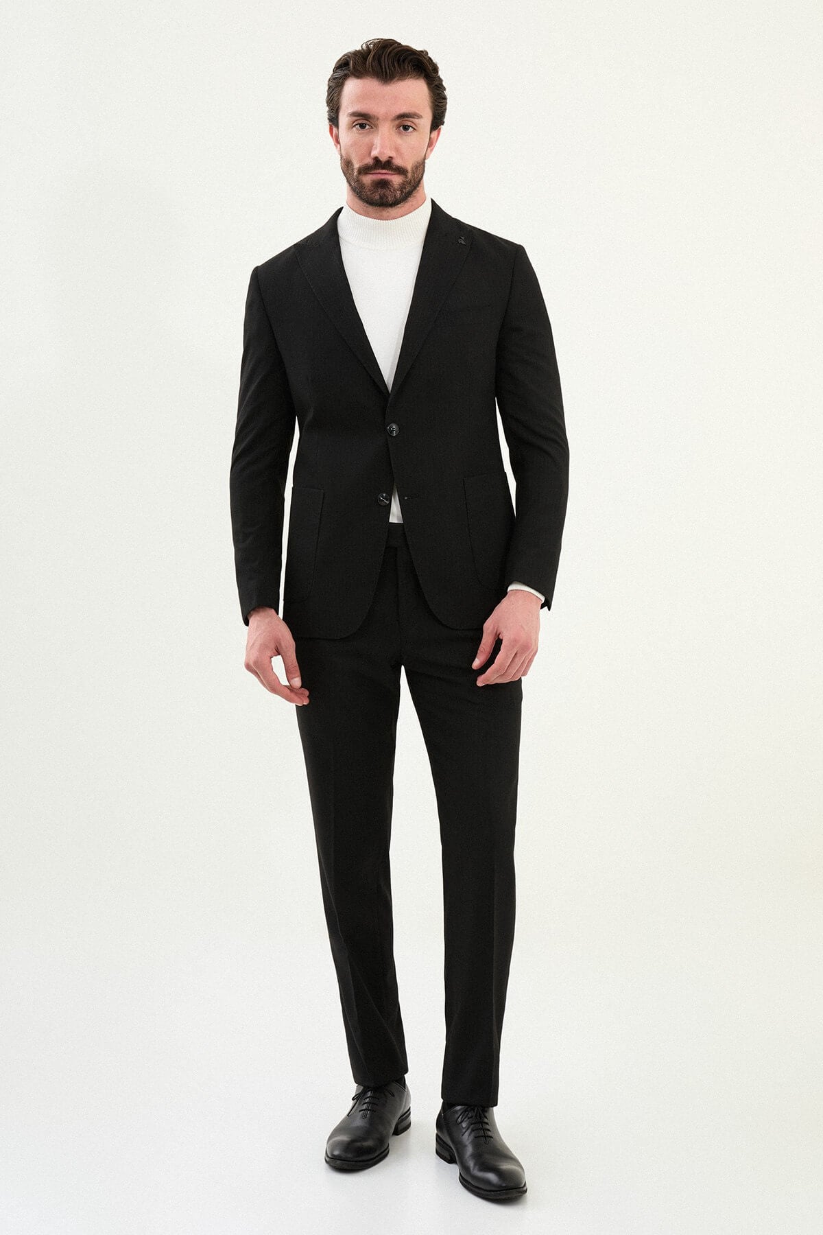 Men’s black mono-collar slim-fit suit with band/mandarin neckline, matte finish tailoring, single-breasted jacket styled with a white turtleneck, travel-ready stretch wool-viscose blend.