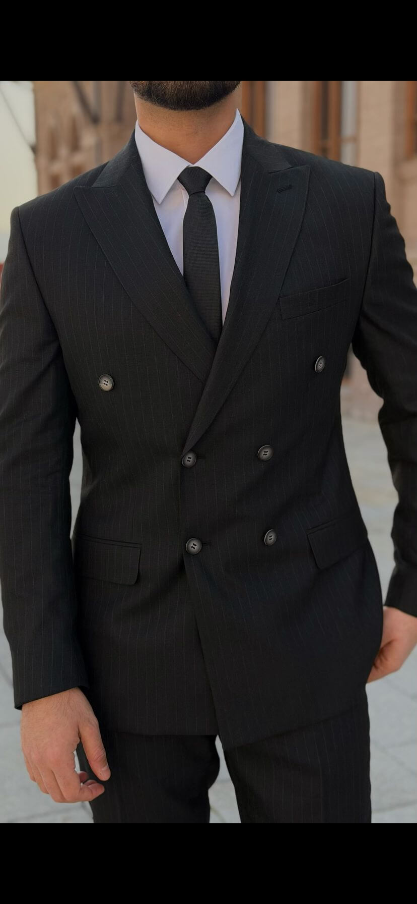 Men’s black double-breasted suit with peak lapel, tailored formal suit styled with white shirt and black tie outdoors
