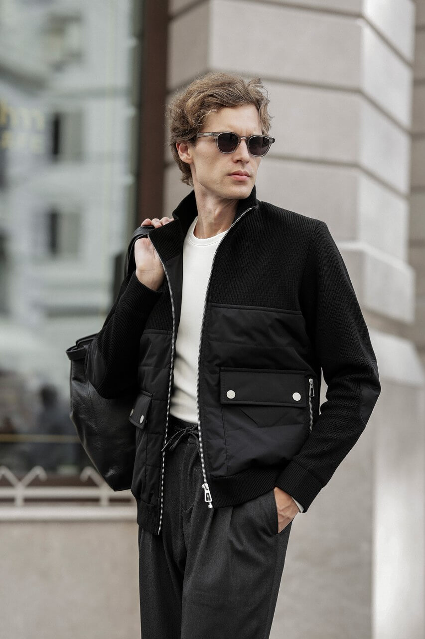 Black men's casual jacket styled with a white T-shirt and grey trousers.