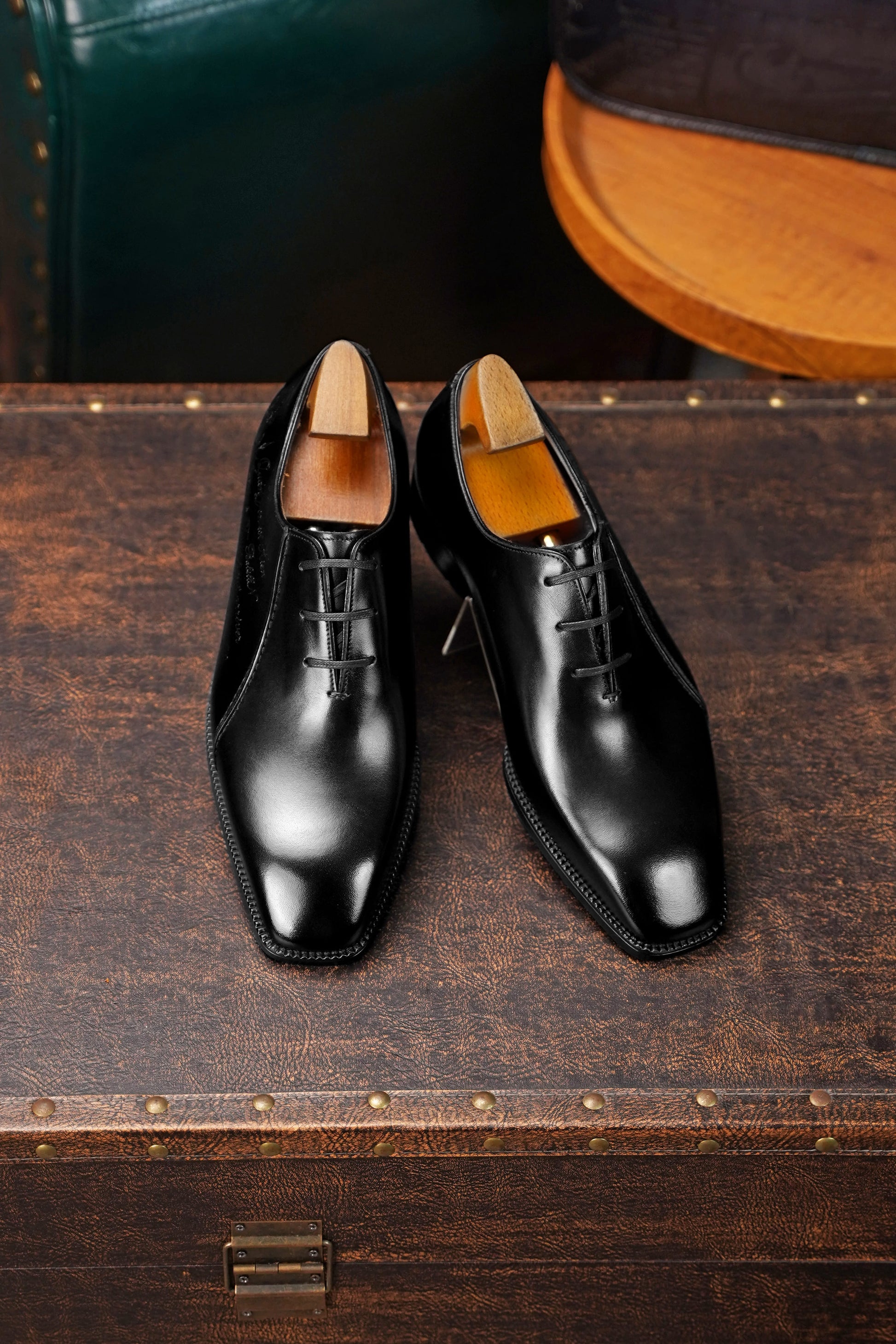 Men’s black leather Oxford dress shoes featuring a polished finish, lace-up closure, sleek pointed toe, and subtle embossed script detailing on the side panel.