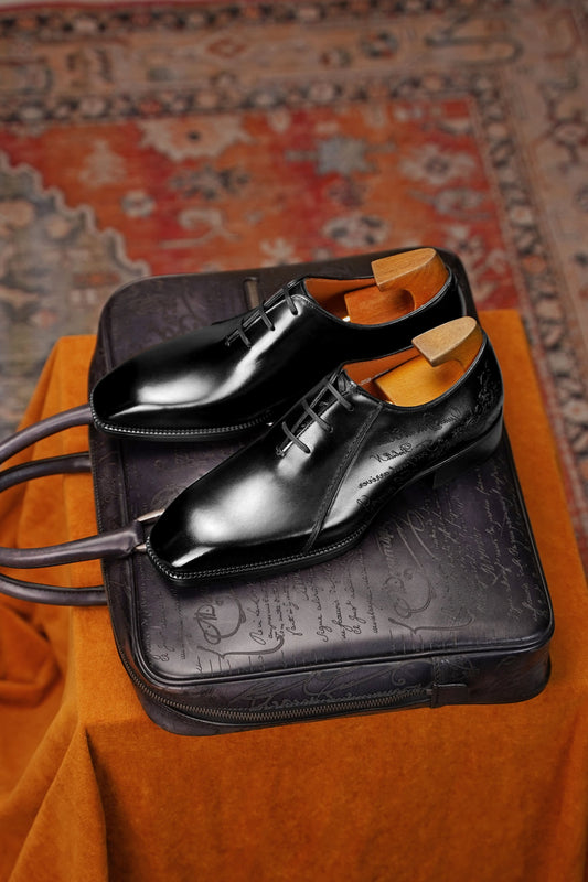 Men’s black leather Oxford dress shoes featuring a polished finish, lace-up closure, sleek pointed toe, and subtle embossed script detailing on the side panel.