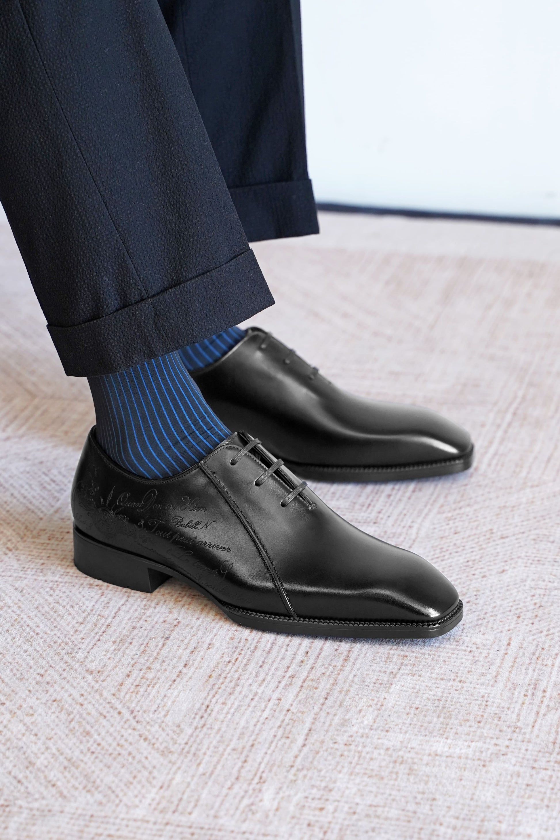 Men’s black leather Oxford dress shoes featuring a polished finish, lace-up closure, sleek pointed toe, and subtle embossed script detailing on the side panel.