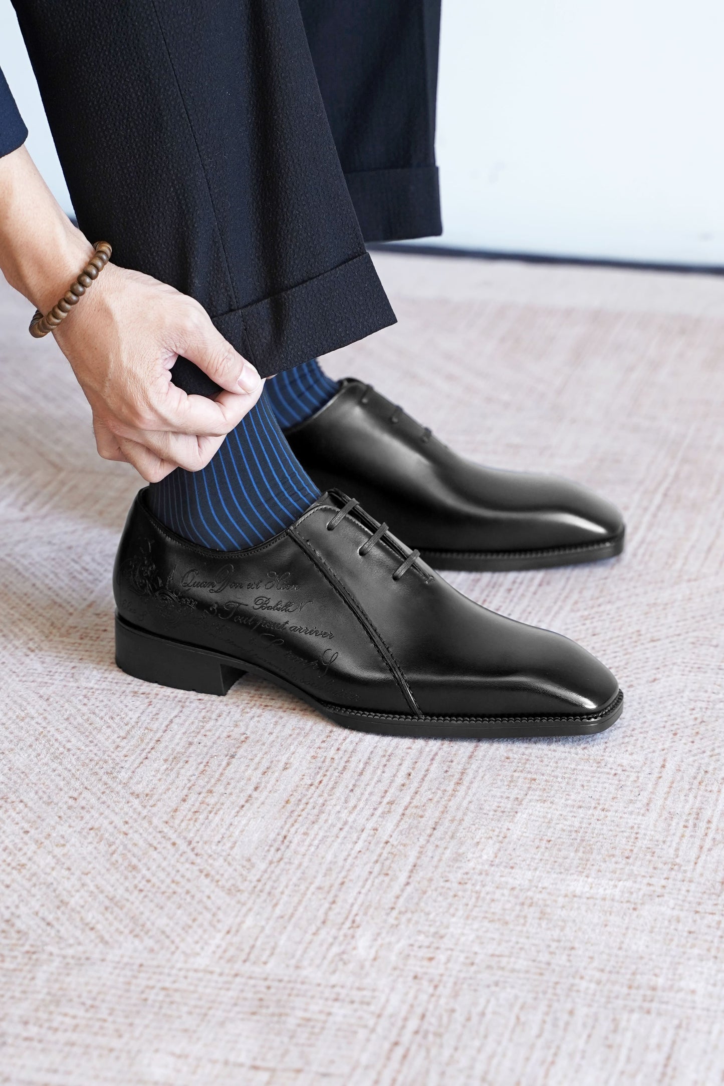 Men’s black leather Oxford dress shoes featuring a polished finish, lace-up closure, sleek pointed toe, and subtle embossed script detailing on the side panel.