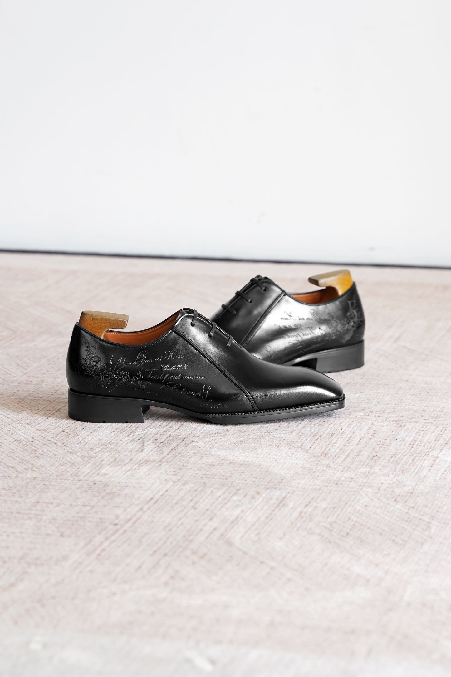 Men’s black leather Oxford dress shoes featuring a polished finish, lace-up closure, sleek pointed toe, and subtle embossed script detailing on the side panel.