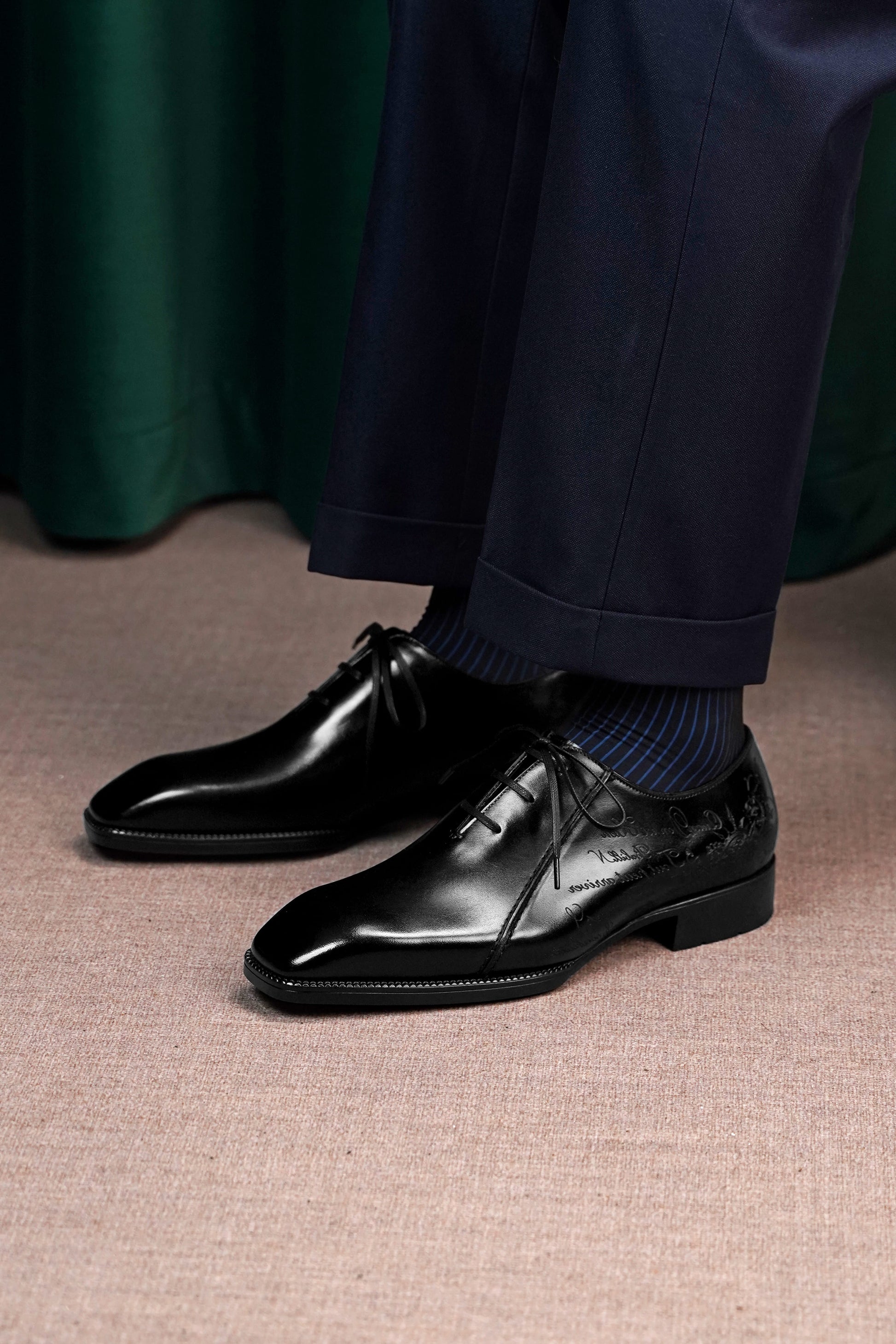 Men’s black leather Oxford dress shoes featuring a polished finish, lace-up closure, sleek pointed toe, and subtle embossed script detailing on the side panel.