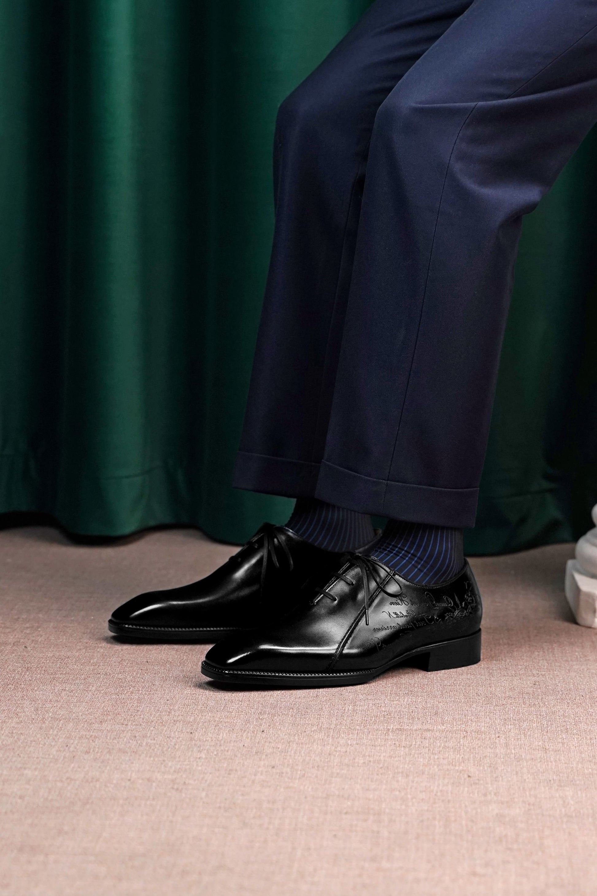 Men’s black leather Oxford dress shoes featuring a polished finish, lace-up closure, sleek pointed toe, and subtle embossed script detailing on the side panel.