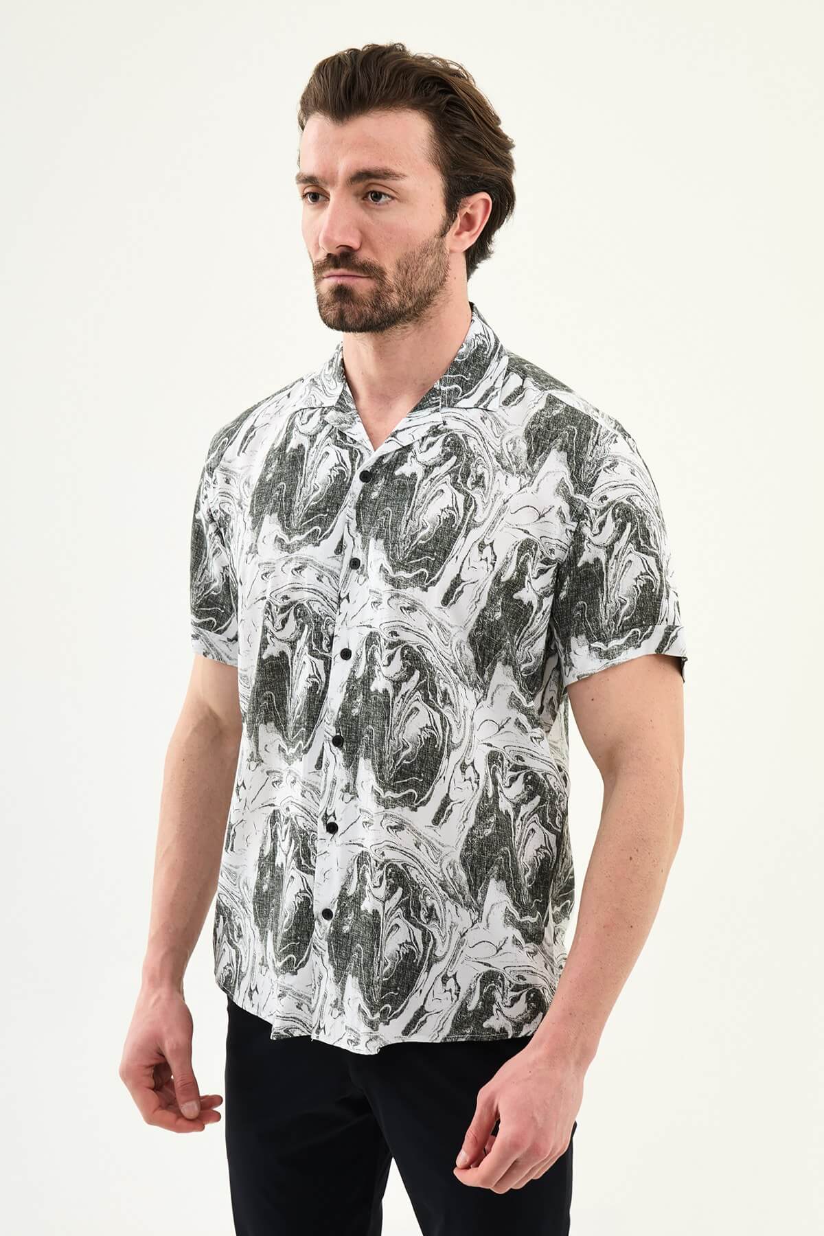 Male model wearing a black-and-white marble print short-sleeve slim fit shirt, styled with black pants, standing against a neutral background, showcasing summer casual fashion.