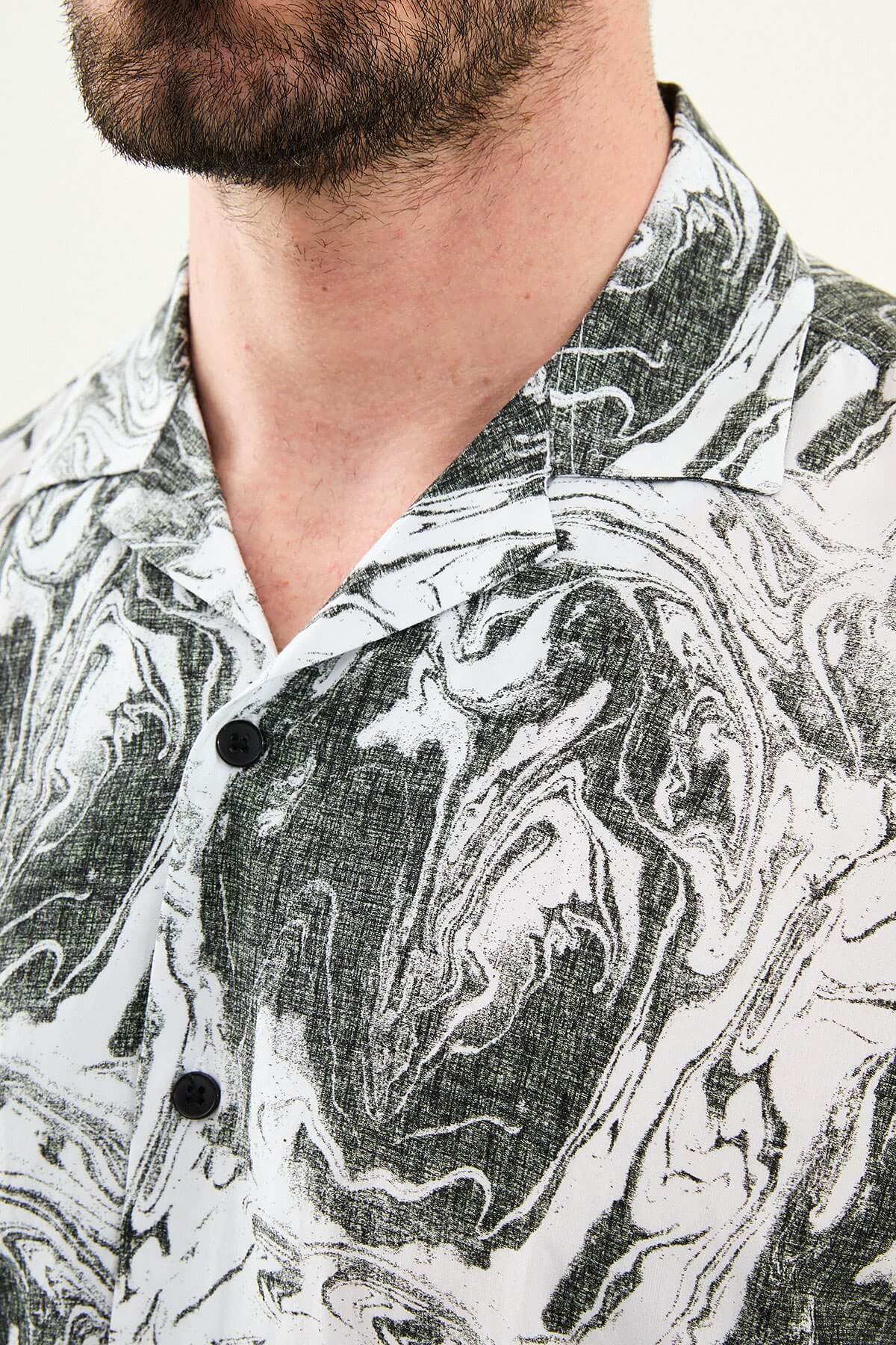Male model wearing a black-and-white marble print short-sleeve slim fit shirt, styled with black pants, standing against a neutral background, showcasing summer casual fashion.