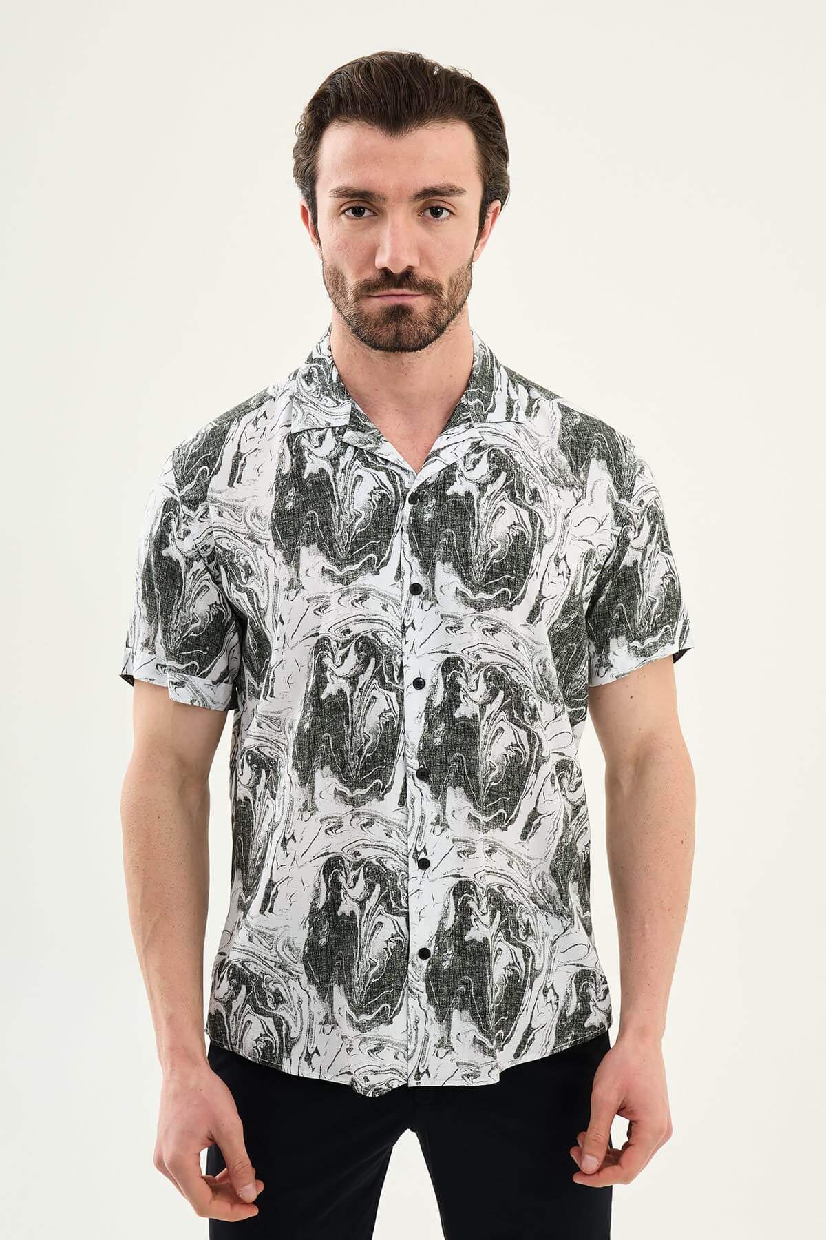 Male model wearing a black-and-white marble print short-sleeve slim fit shirt, styled with black pants, standing against a neutral background, showcasing summer casual fashion.