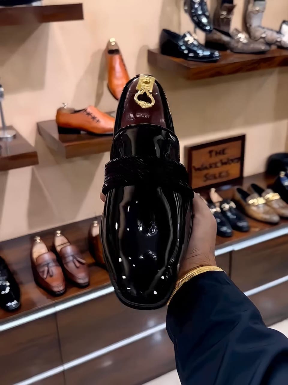 Black patent leather loafers with a glossy finish and woven strap detail, styled for both formal and semi-formal occasions.
