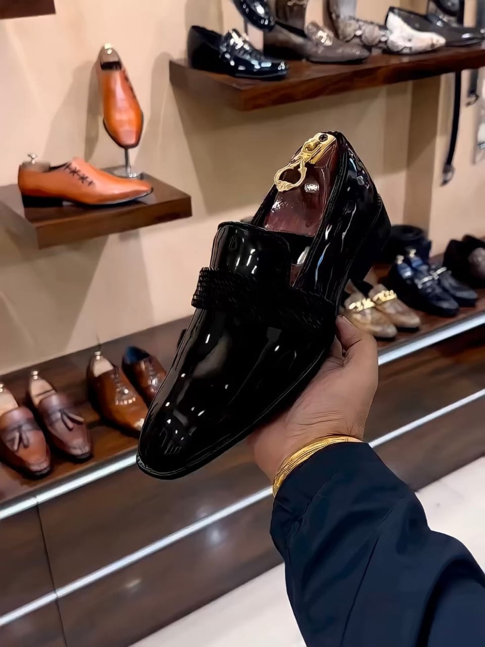 Black patent leather loafers with a glossy finish and woven strap detail, styled for both formal and semi-formal occasions.