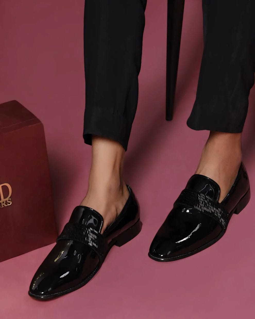 Black patent leather loafers with a glossy finish and woven strap detail, styled for both formal and semi-formal occasions.
