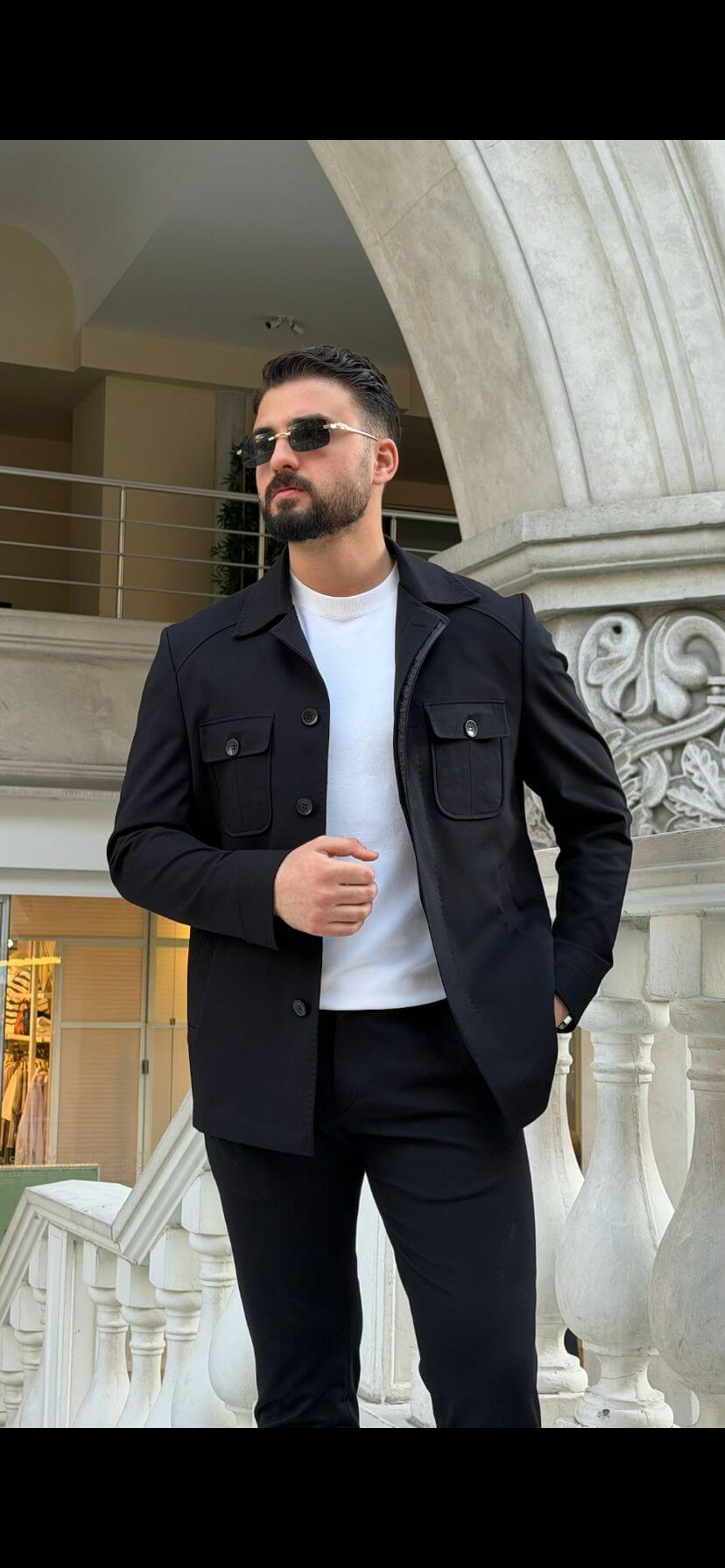 Men’s black safari co-set with buttoned jacket and multiple pockets, paired with black pants and white t-shirt, worn casually outdoors.