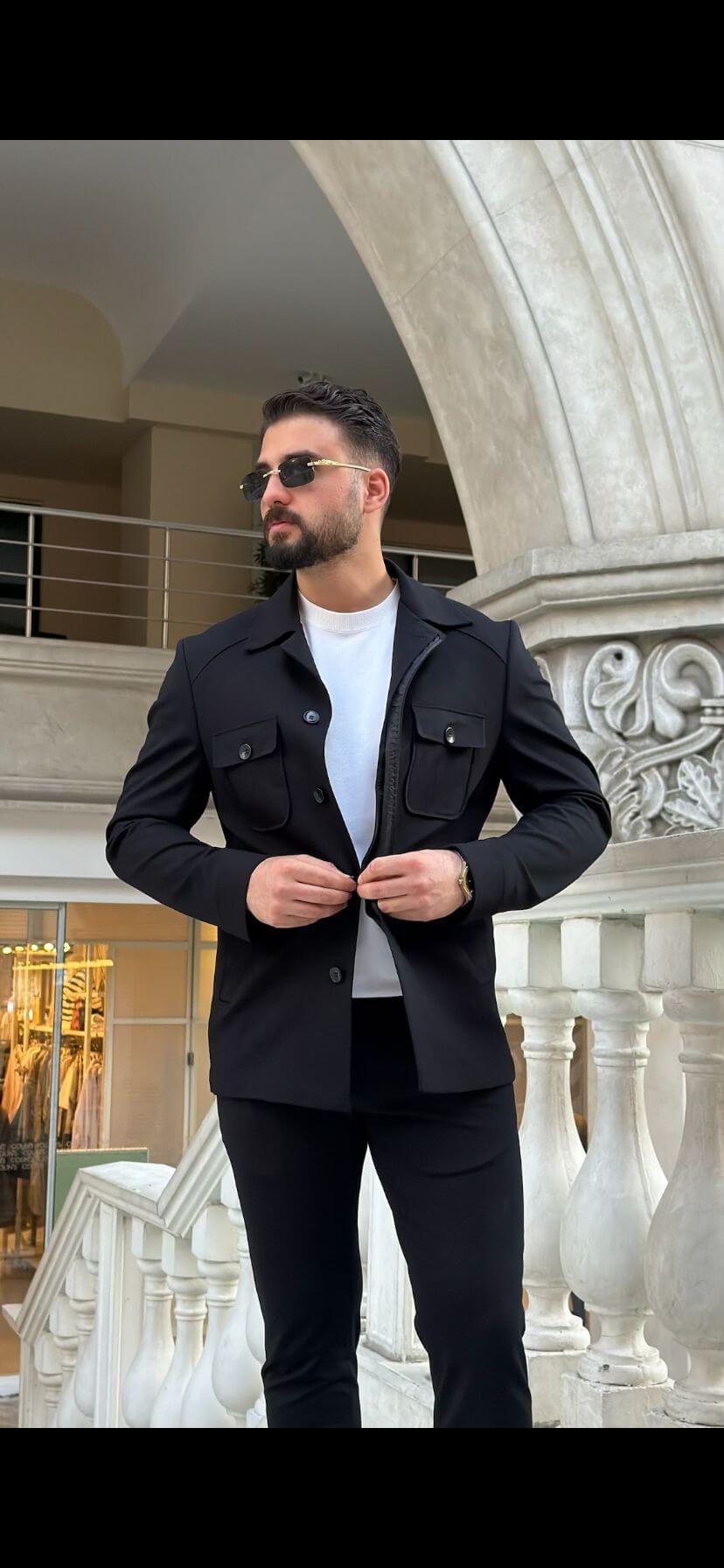 Men’s black safari co-set with buttoned jacket and multiple pockets, paired with black pants and white t-shirt, worn casually outdoors.