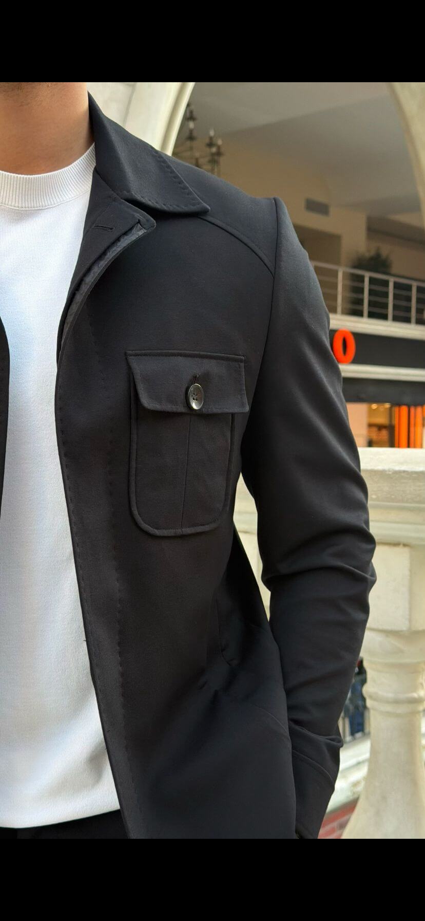 Men’s black safari co-set with buttoned jacket and multiple pockets, paired with black pants and white t-shirt, worn casually outdoors.