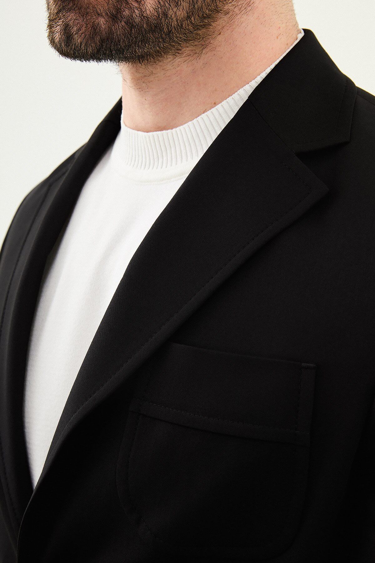 Close-up of a men's black slim fit single-breasted blazer with notched lapels and front pockets, styled over a white shirt for a modern formal look.