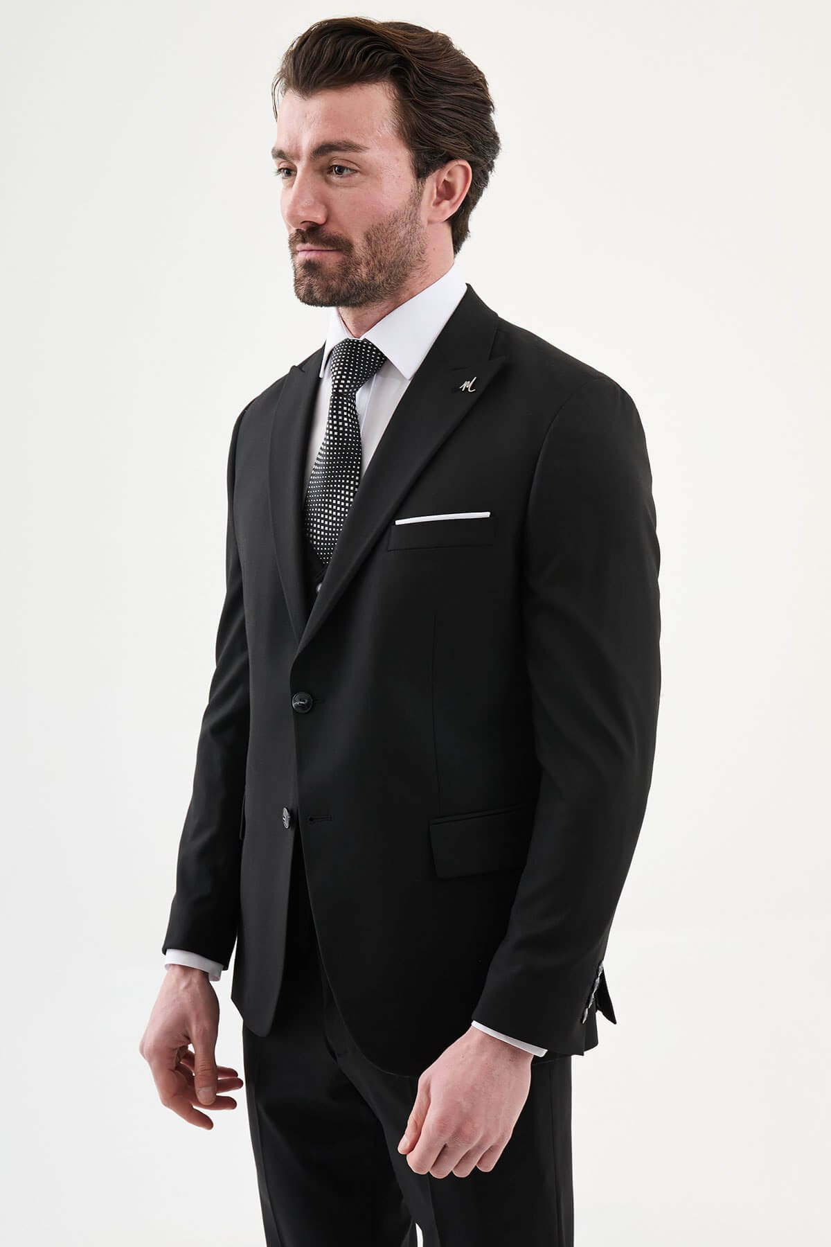 man wearing a black slim-fit three-piece suit, including blazer, waistcoat, and trousers, styled with a white dress shirt and black tie, suitable for formal events or weddings.