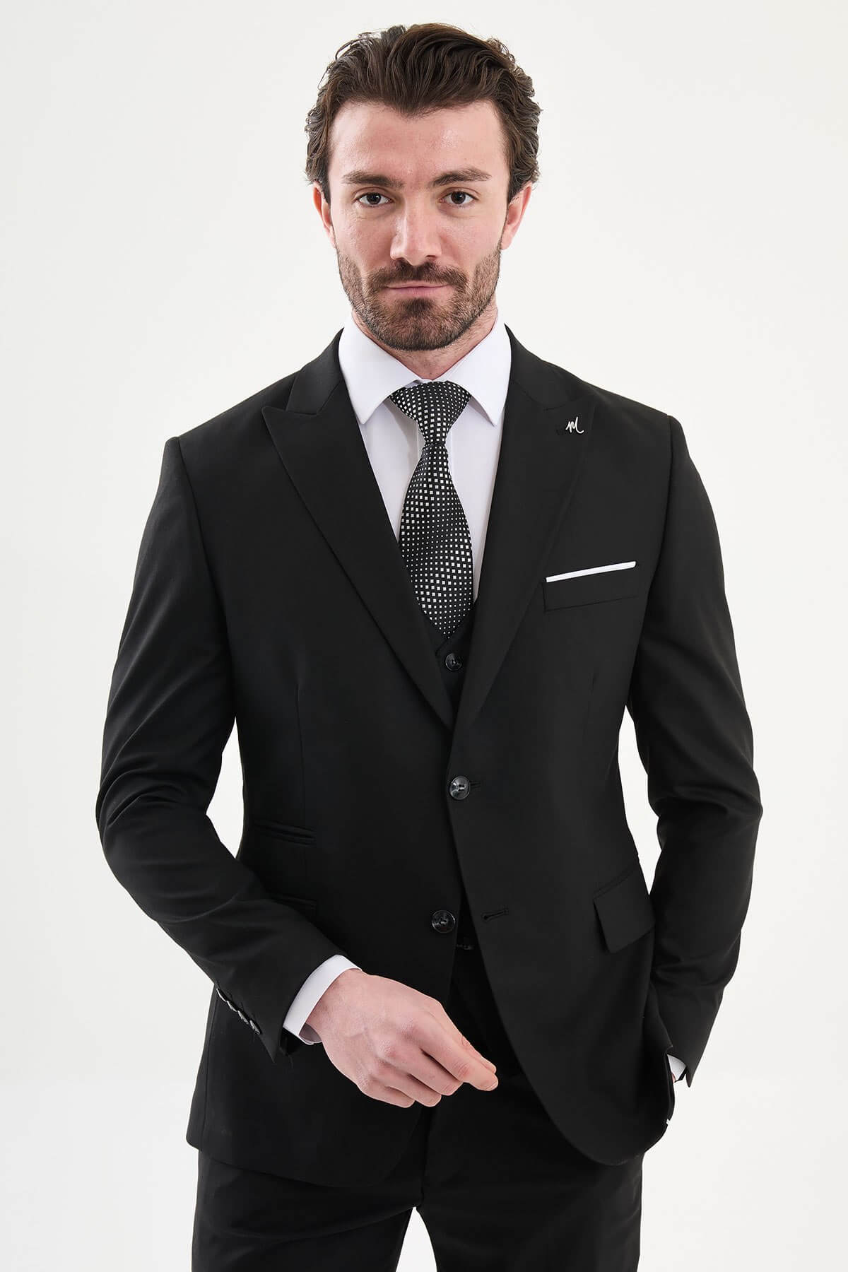 man wearing a black slim-fit three-piece suit, including blazer, waistcoat, and trousers, styled with a white dress shirt and black tie, suitable for formal events or weddings.