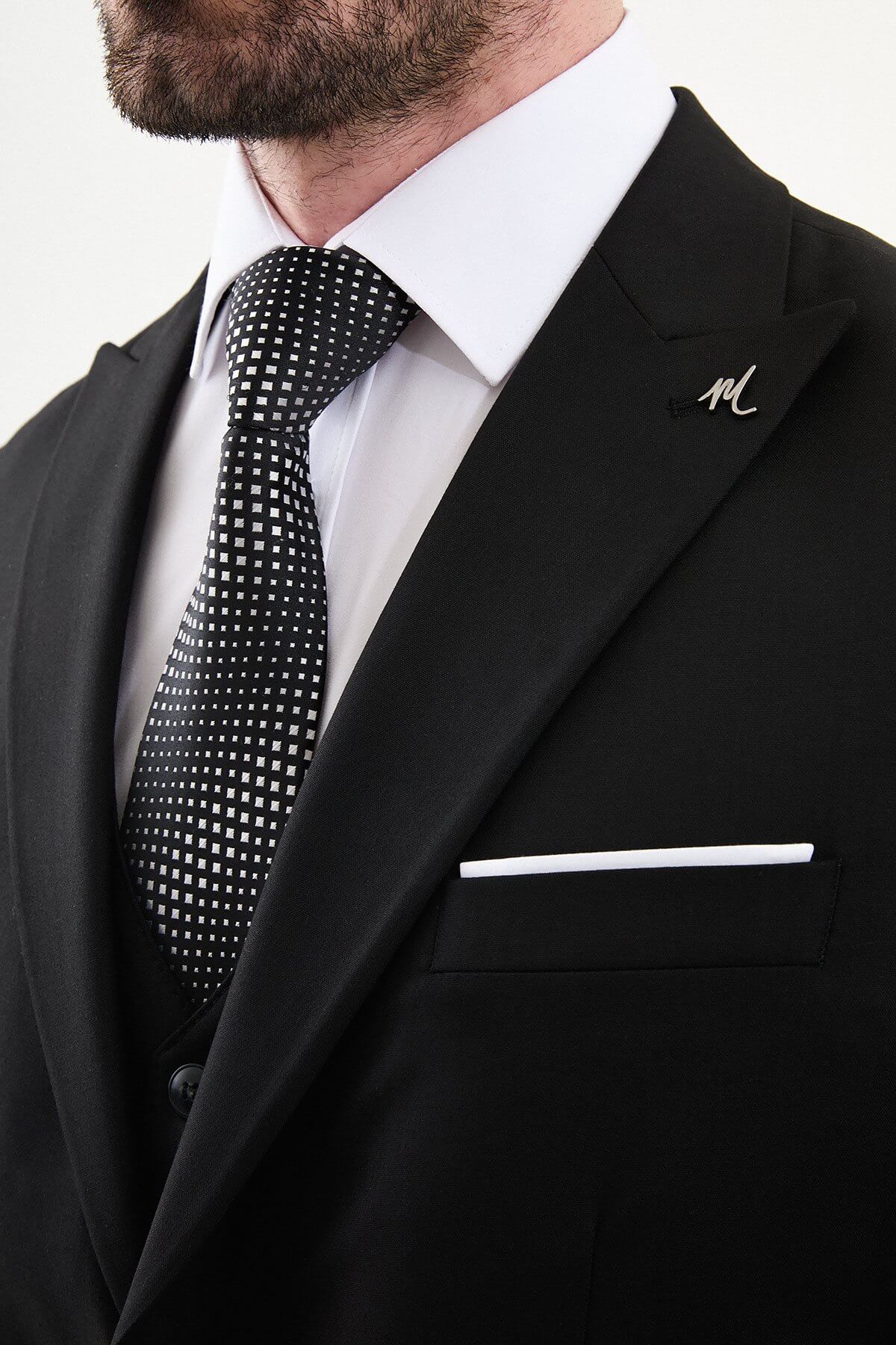 man wearing a black slim-fit three-piece suit, including blazer, waistcoat, and trousers, styled with a white dress shirt and black tie, suitable for formal events or weddings.