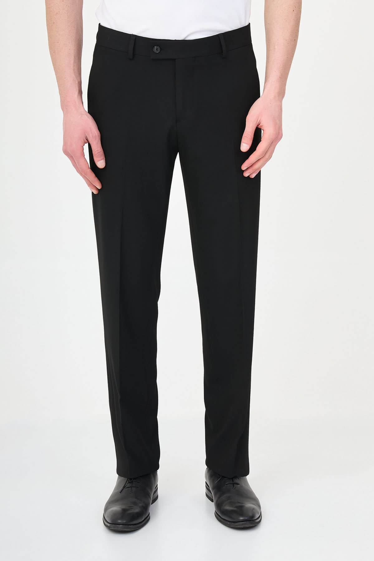 Man wearing black pleated dress trousers with straight slim fit, styled with a white dress shirt and black leather shoes.