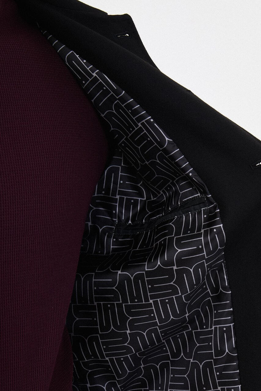 Men's black fall/winter utility jacket styled with a burgundy crew-neck shirt and black trousers.